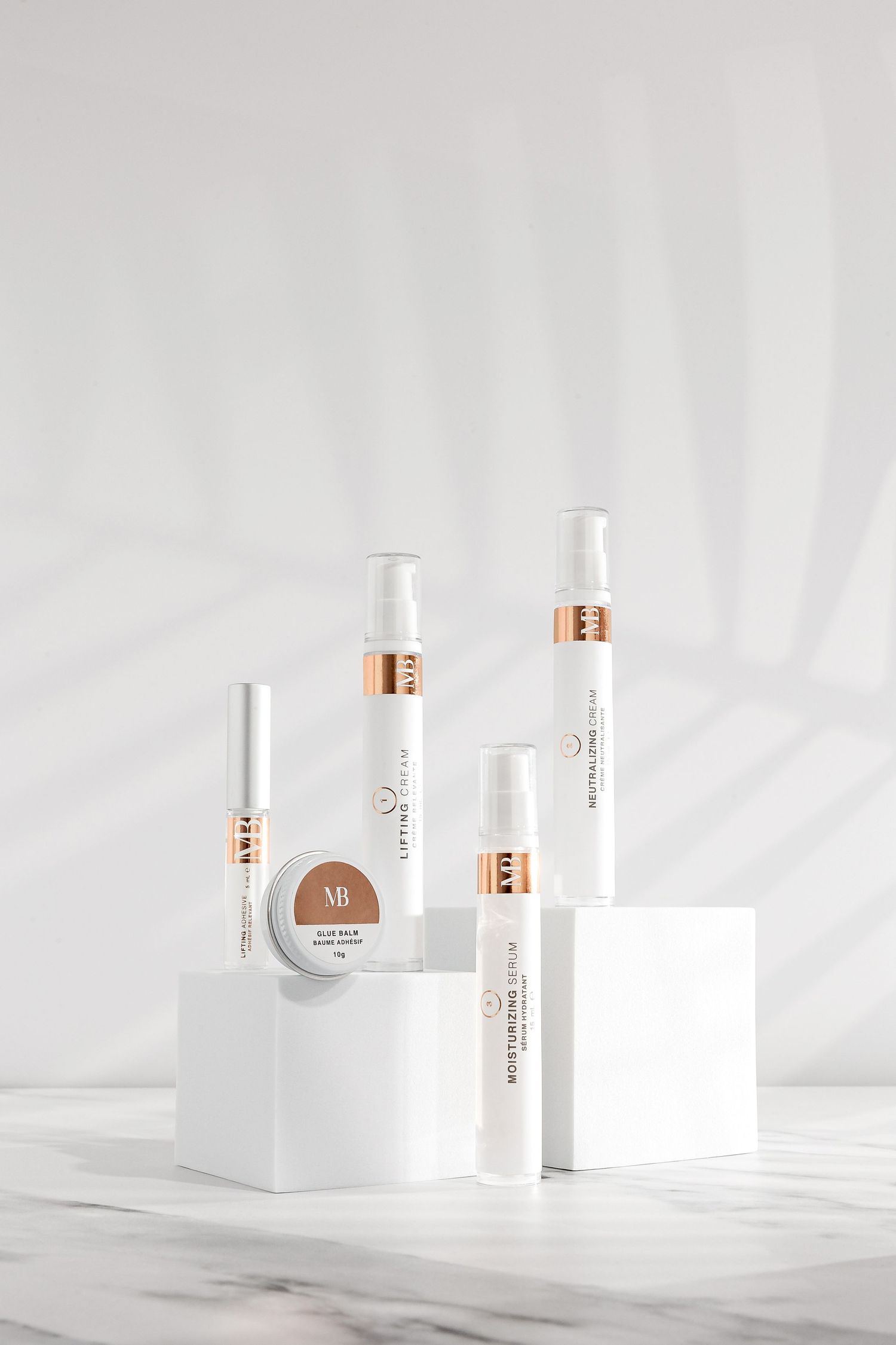 Minimalist white beauty products with copper accents arranged on marble surface.