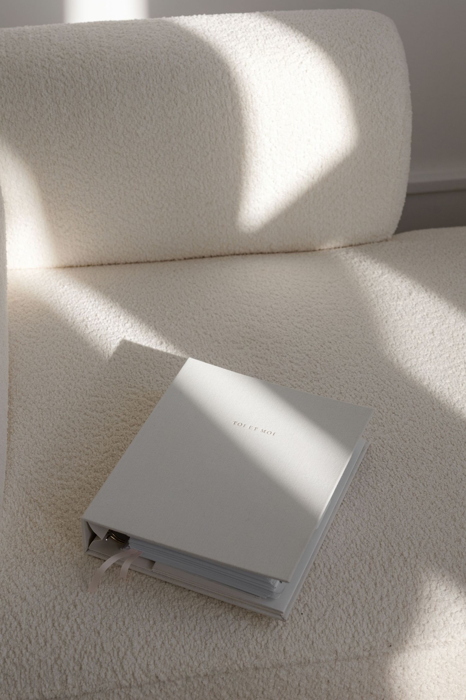 White book lying on textured white surface with dramatic window light and shadows.