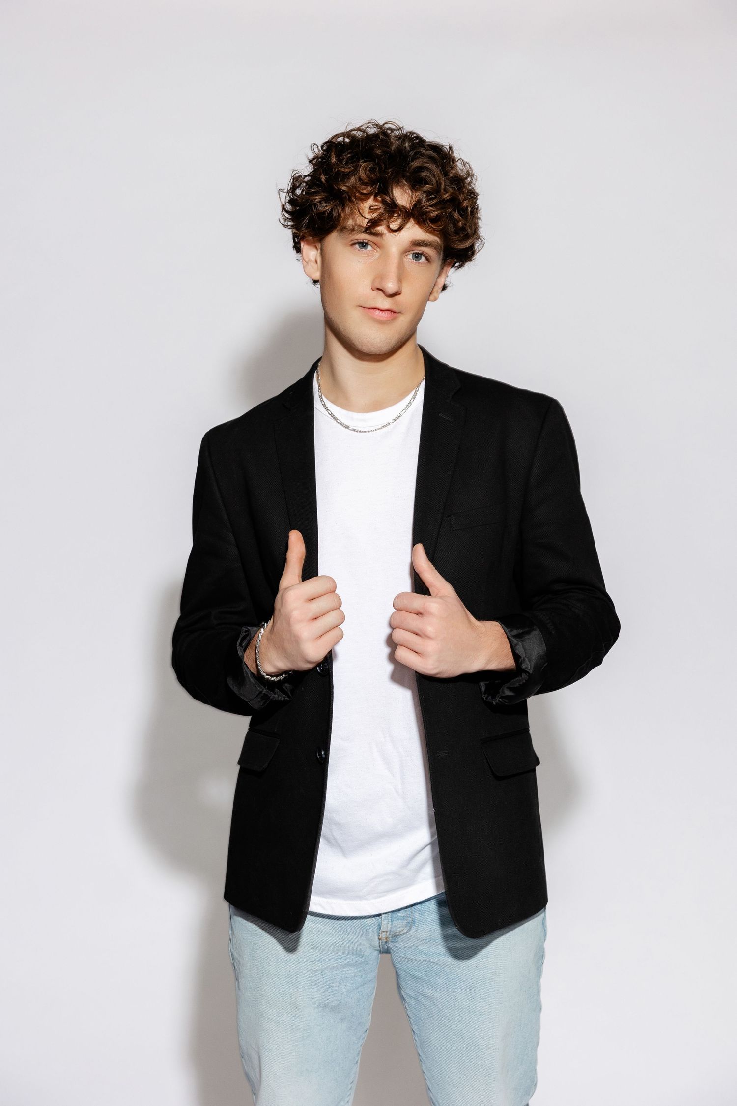 Young man in black blazer and white t-shirt poses against white background.