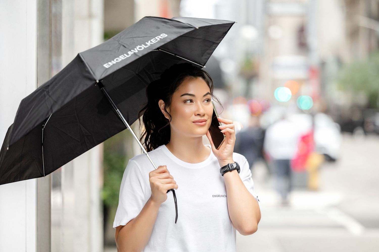 Person holding a black umbrella while walking down a city street.