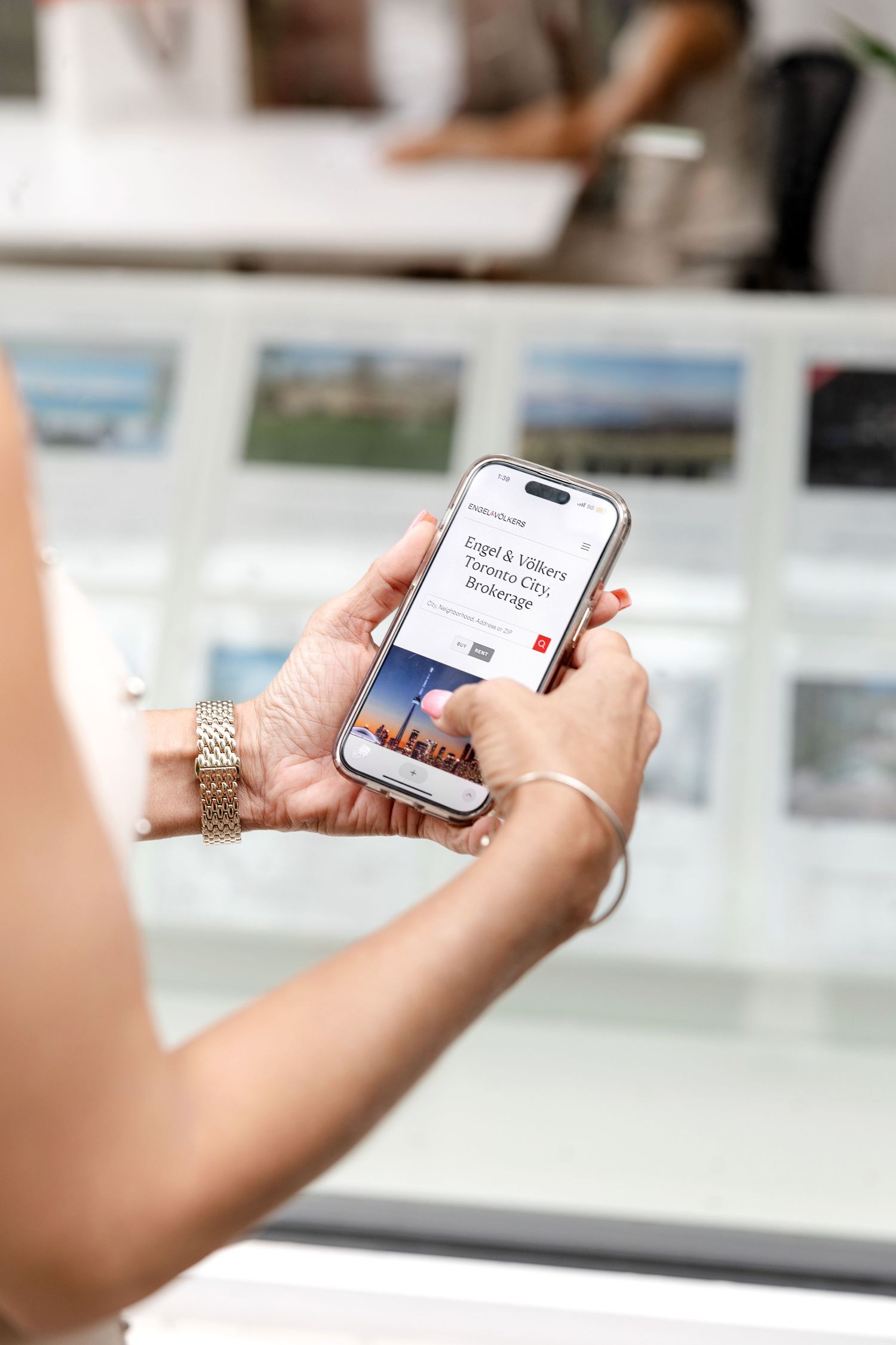 Hand holding smartphone displaying real estate property listings on screen.