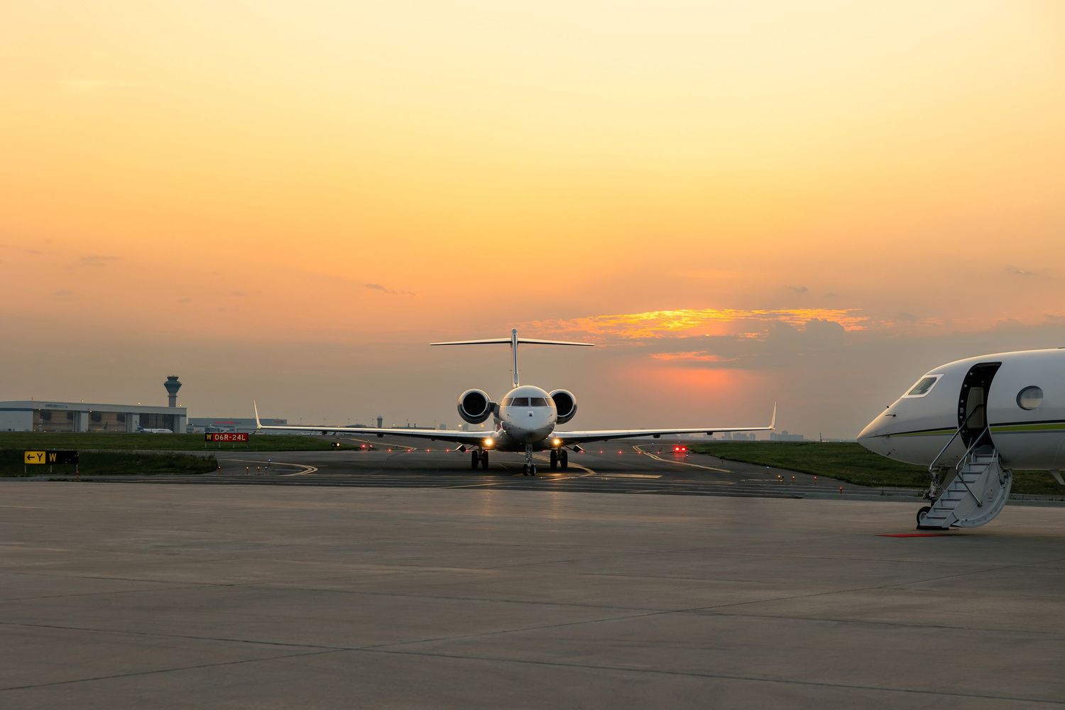 Private jet parked on tarmac during golden sunset with orange sky.