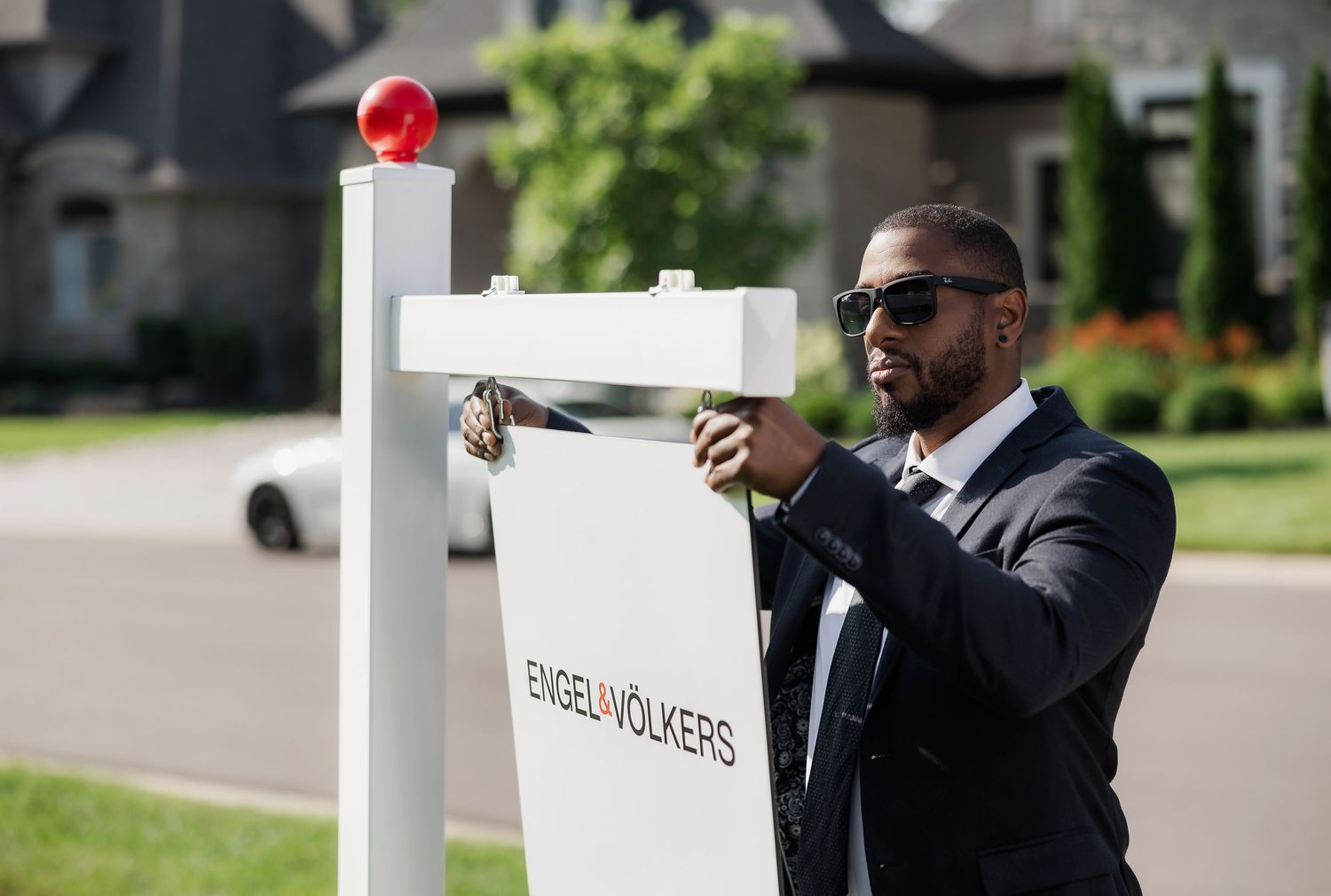 Real estate agent installing for sale sign on white post in front yard.