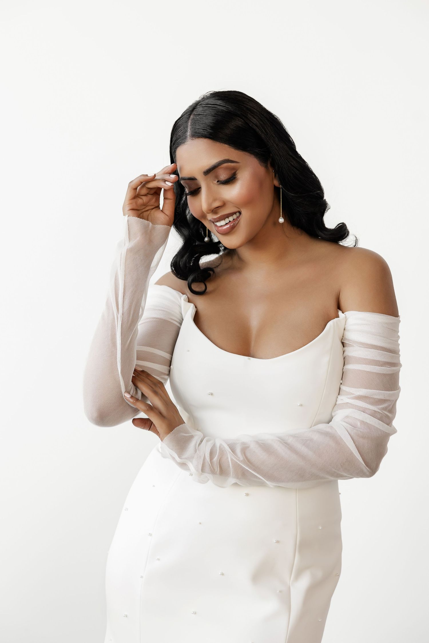 Model wearing white off-shoulder sweater poses elegantly against white background.