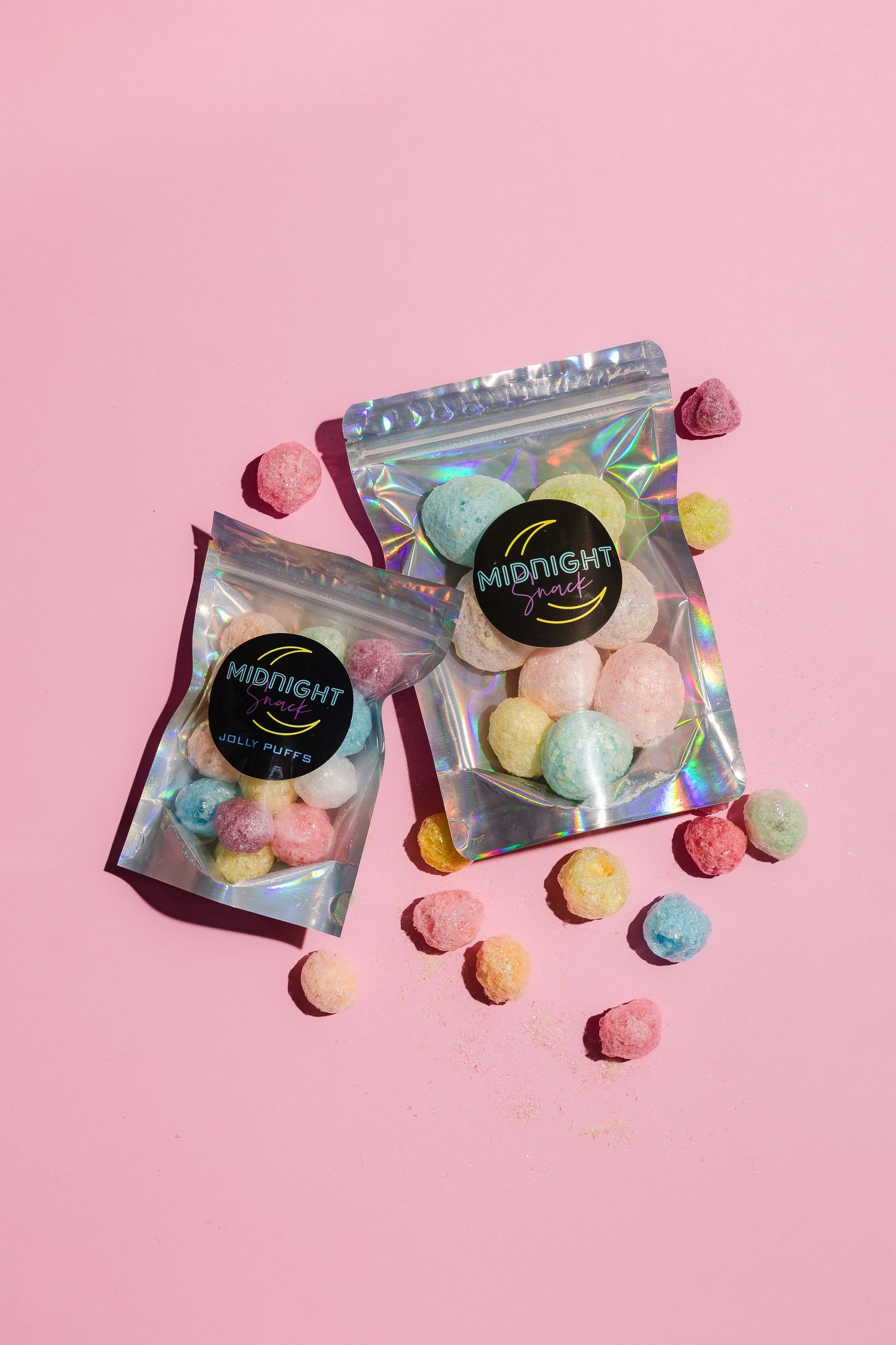 Colorful candy packages with holographic design displayed on pink background.