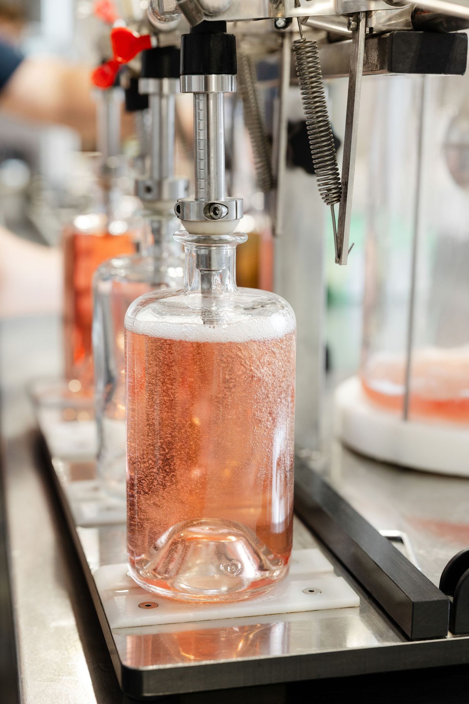 Pink liquid being bottled in manufacturing facility with industrial equipment.