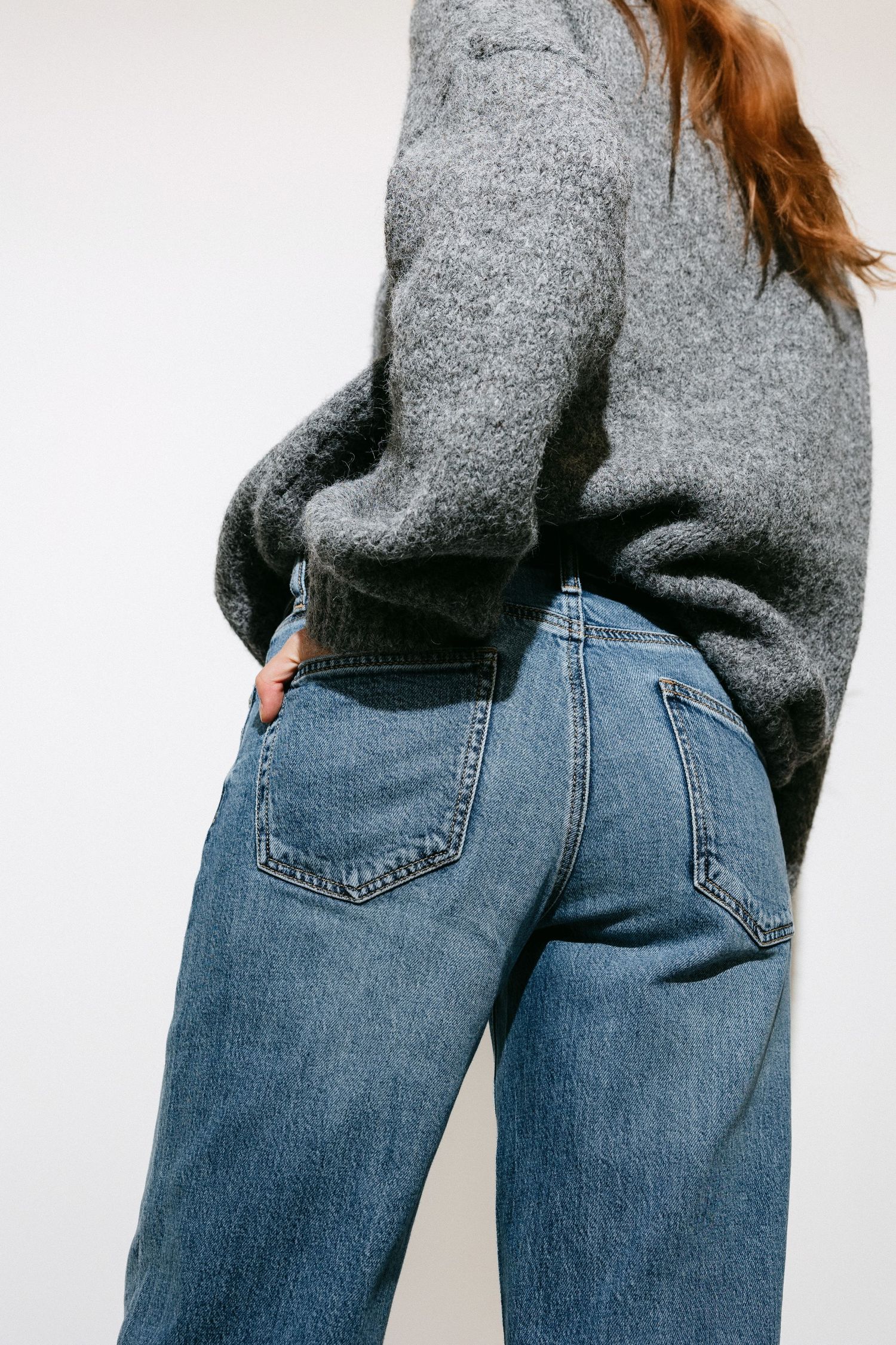 Close-up detail shot of blue jeans pockets and grey sweater combination.