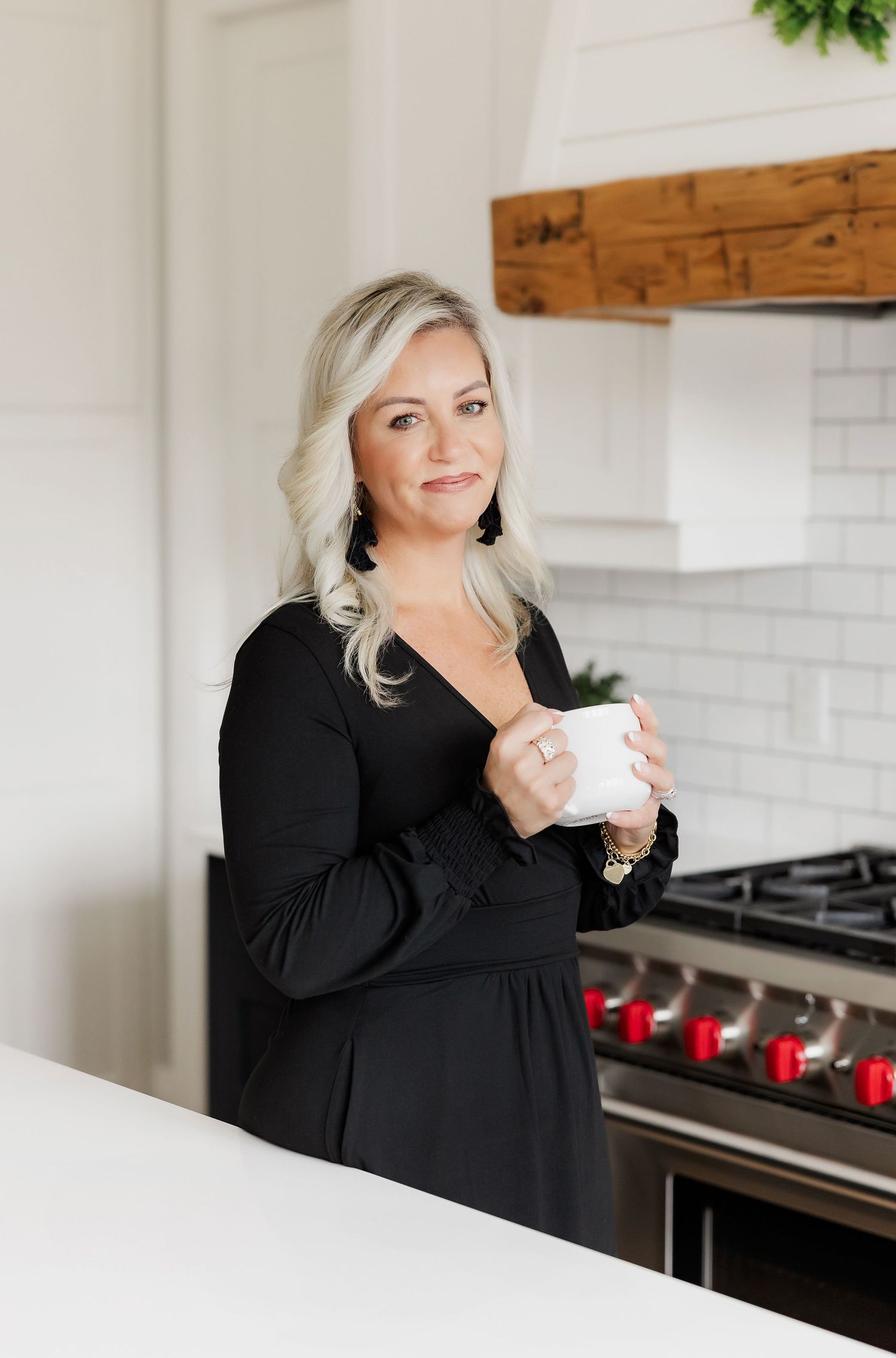 Person in black dress enjoying coffee at modern white kitchen counter with pendant lighting.