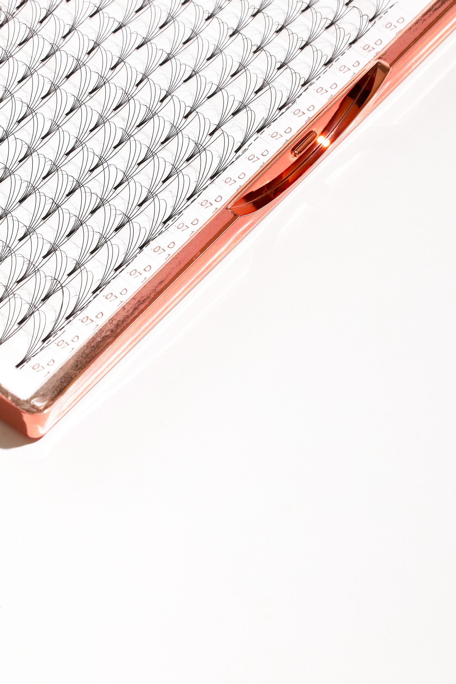 Close-up view of individual eyelash extensions arranged in neat rows with rose gold tweezers.