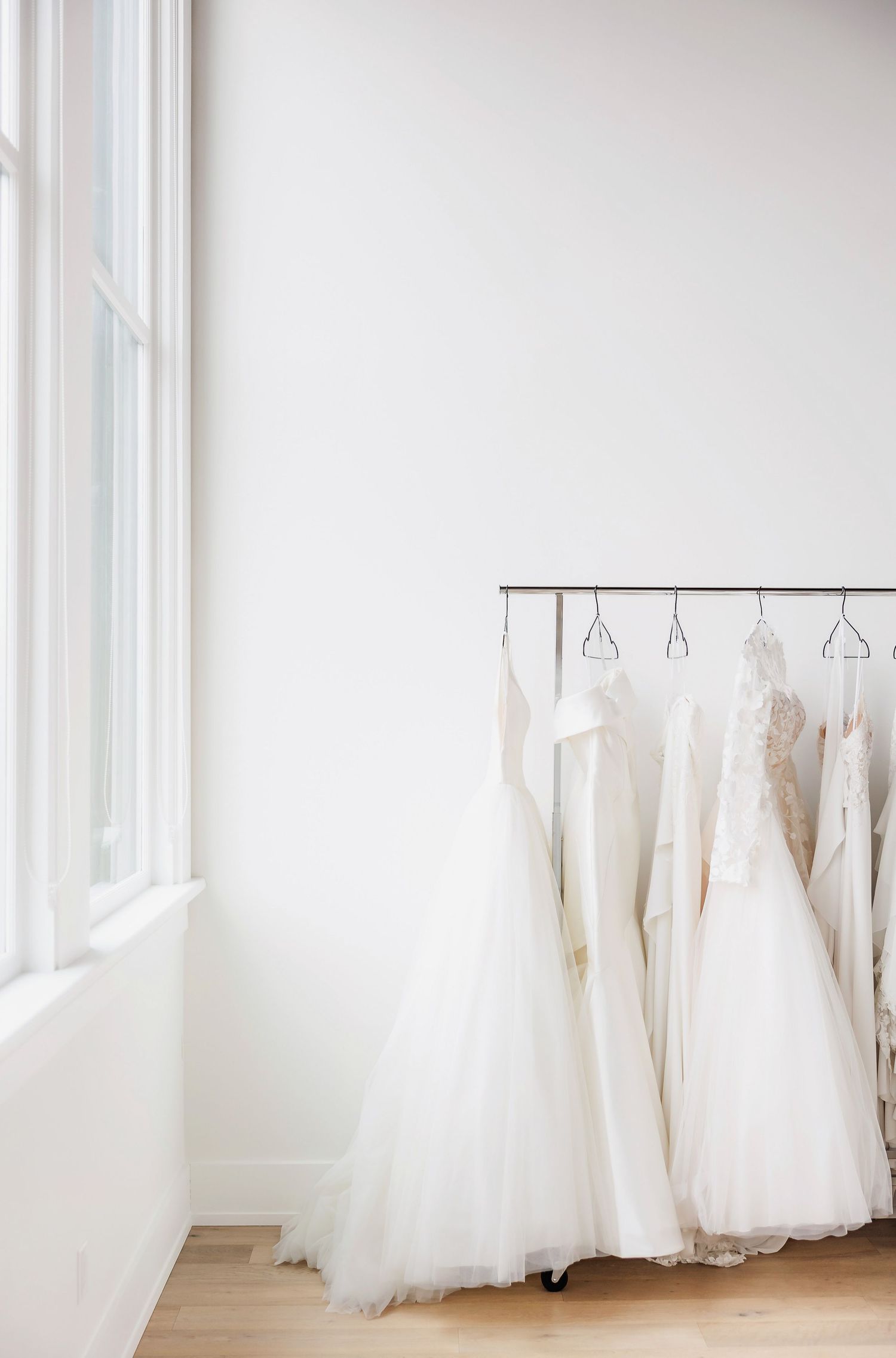Row of elegant white wedding gowns displayed in a bright, minimalist showroom.