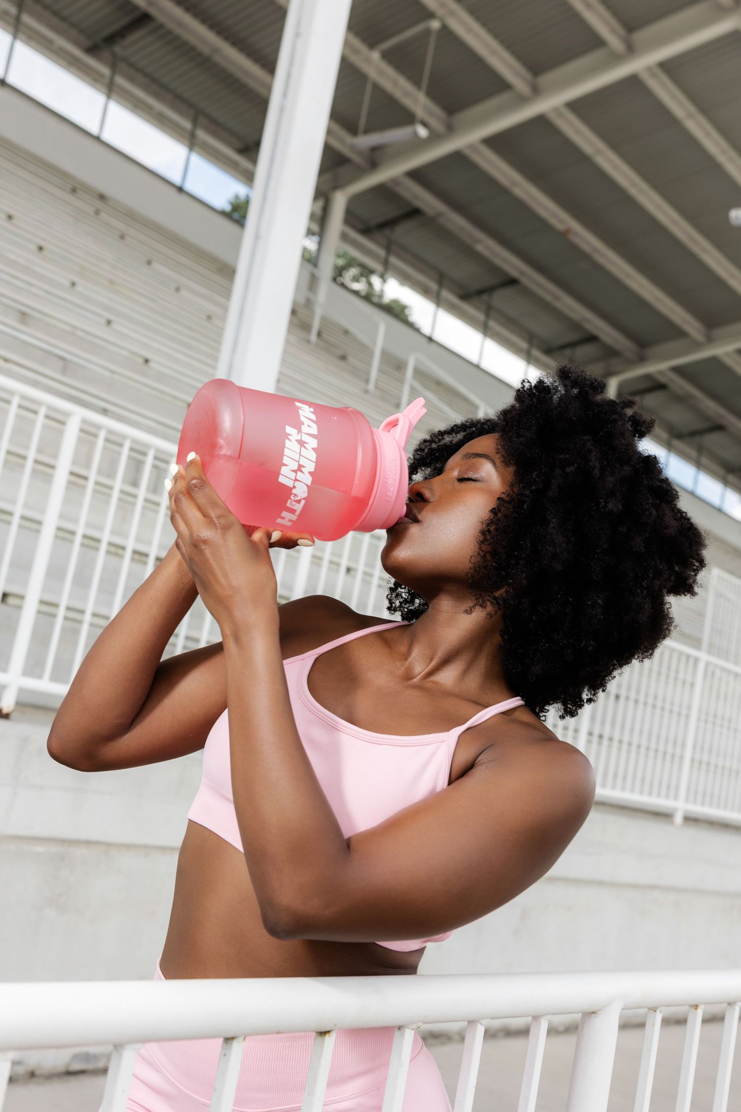 Athletic woman in pink workout top drinking from a red water bottle during exercise.