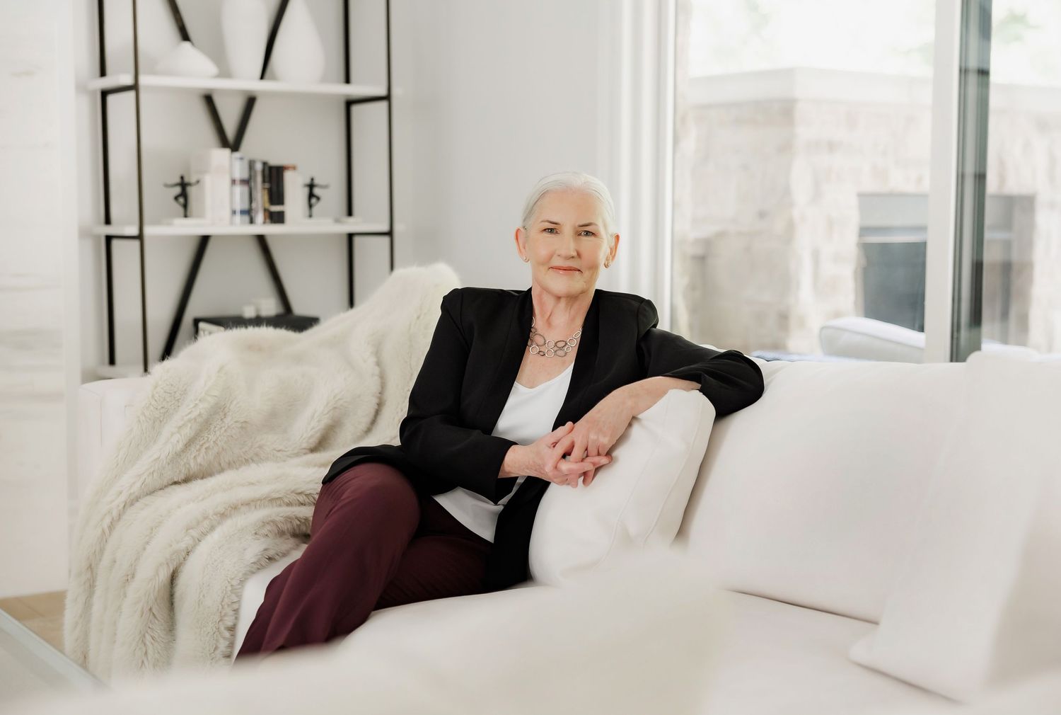 Professional realtor in business attire relaxes on white couch in modern bright office setting.