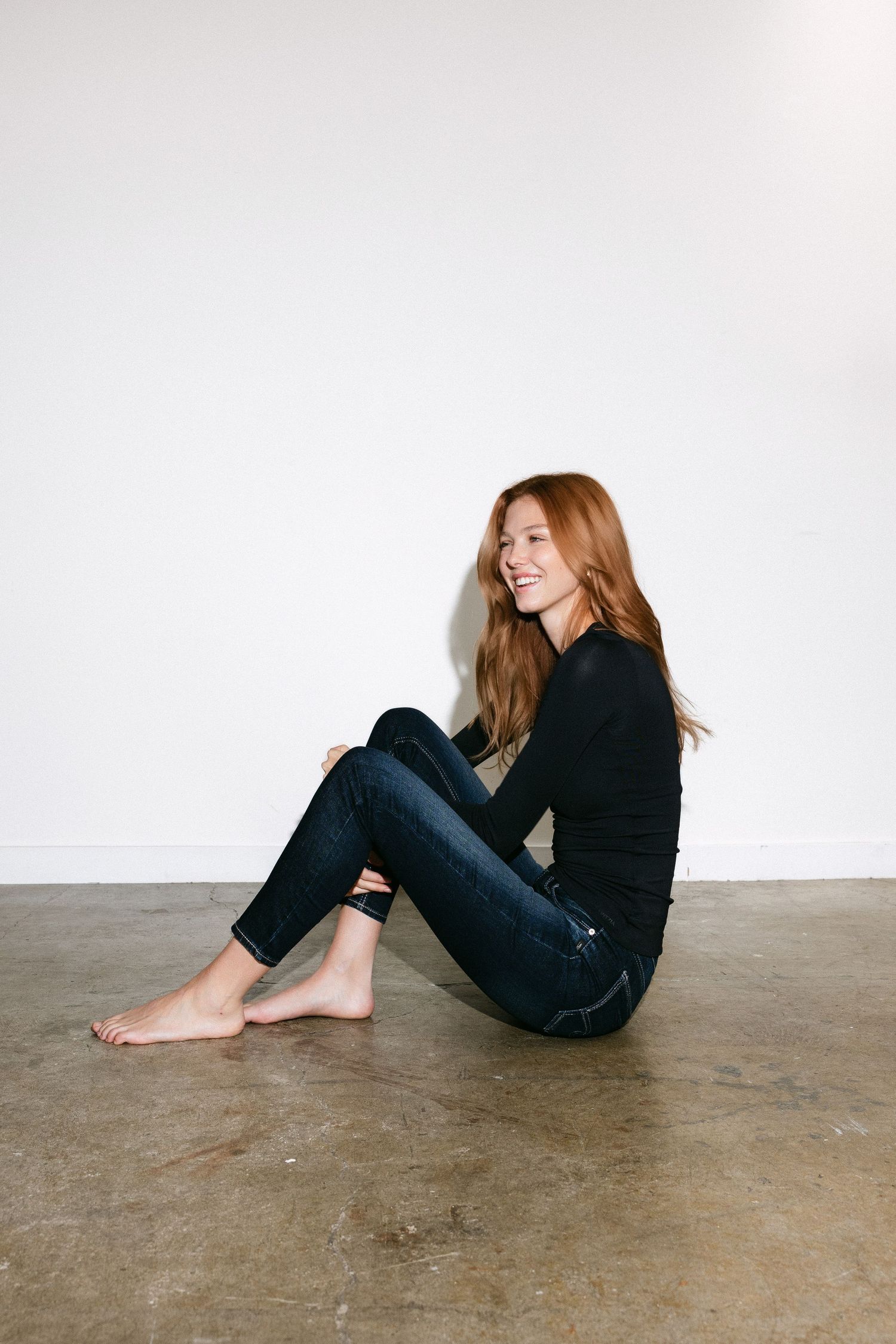 Casual lounging poses showing black sweater and jeans on concrete floor.