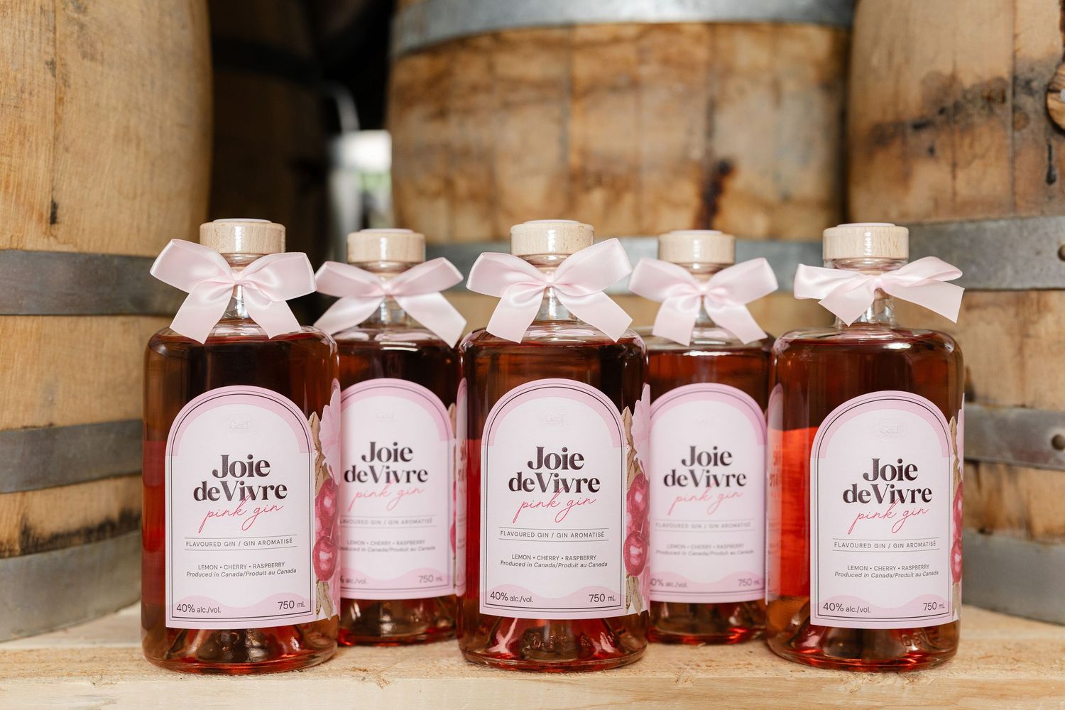Multiple bottles of Joie de Vivre pink beverage displayed on wooden barrel.