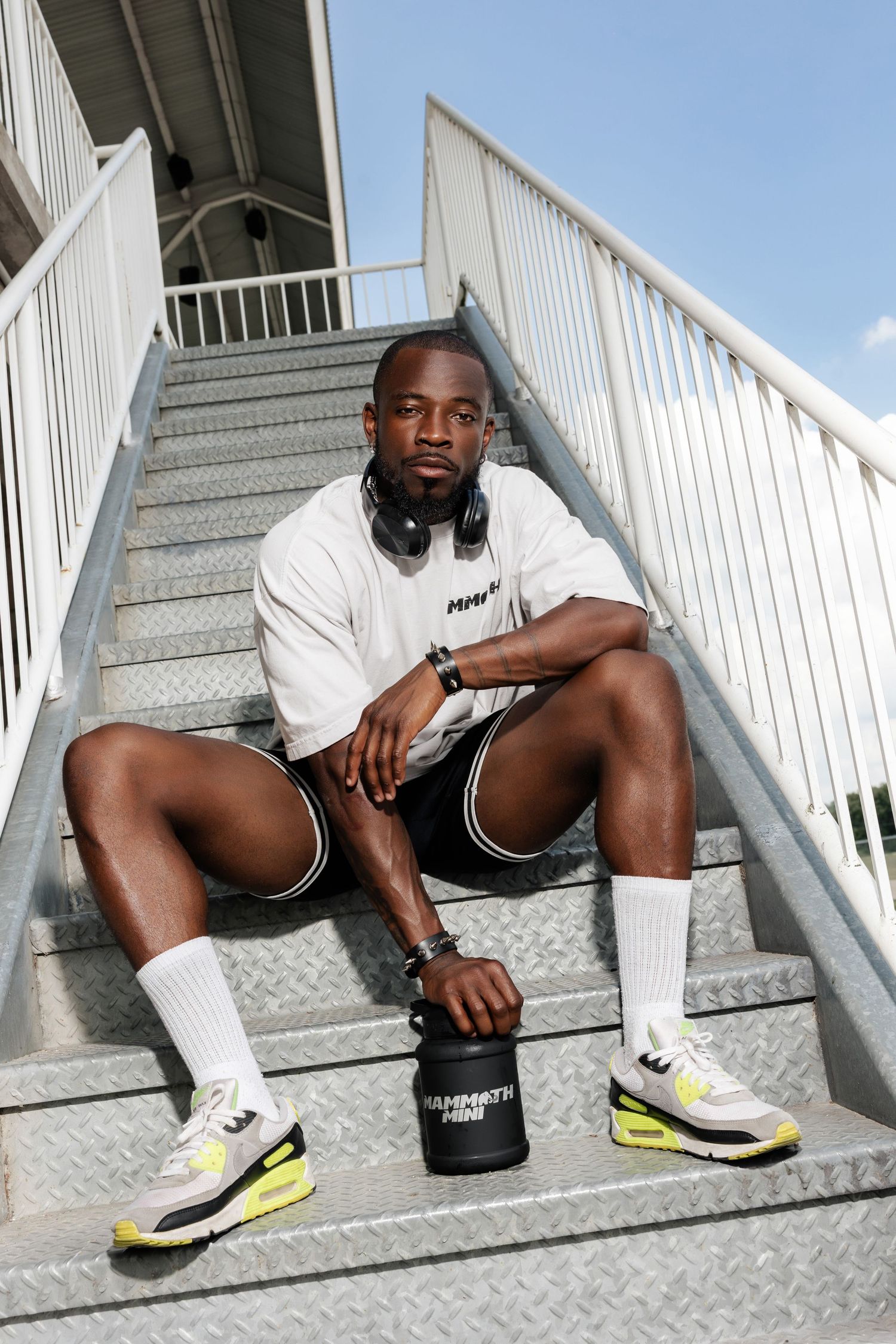 Person in casual sportswear sitting on industrial stairs with headphones.