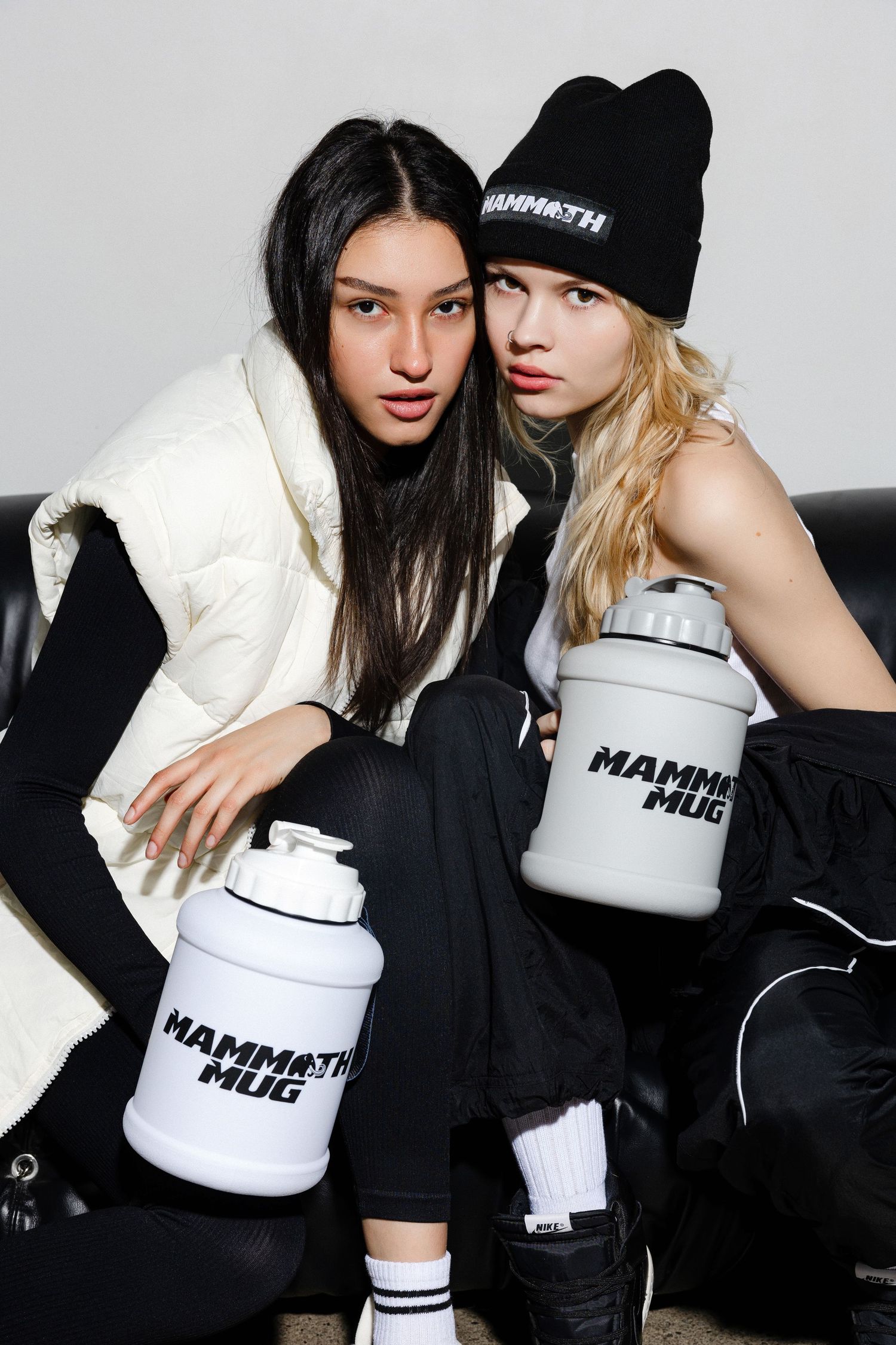 Models in black and white outfits pose with white branded containers against a light background.