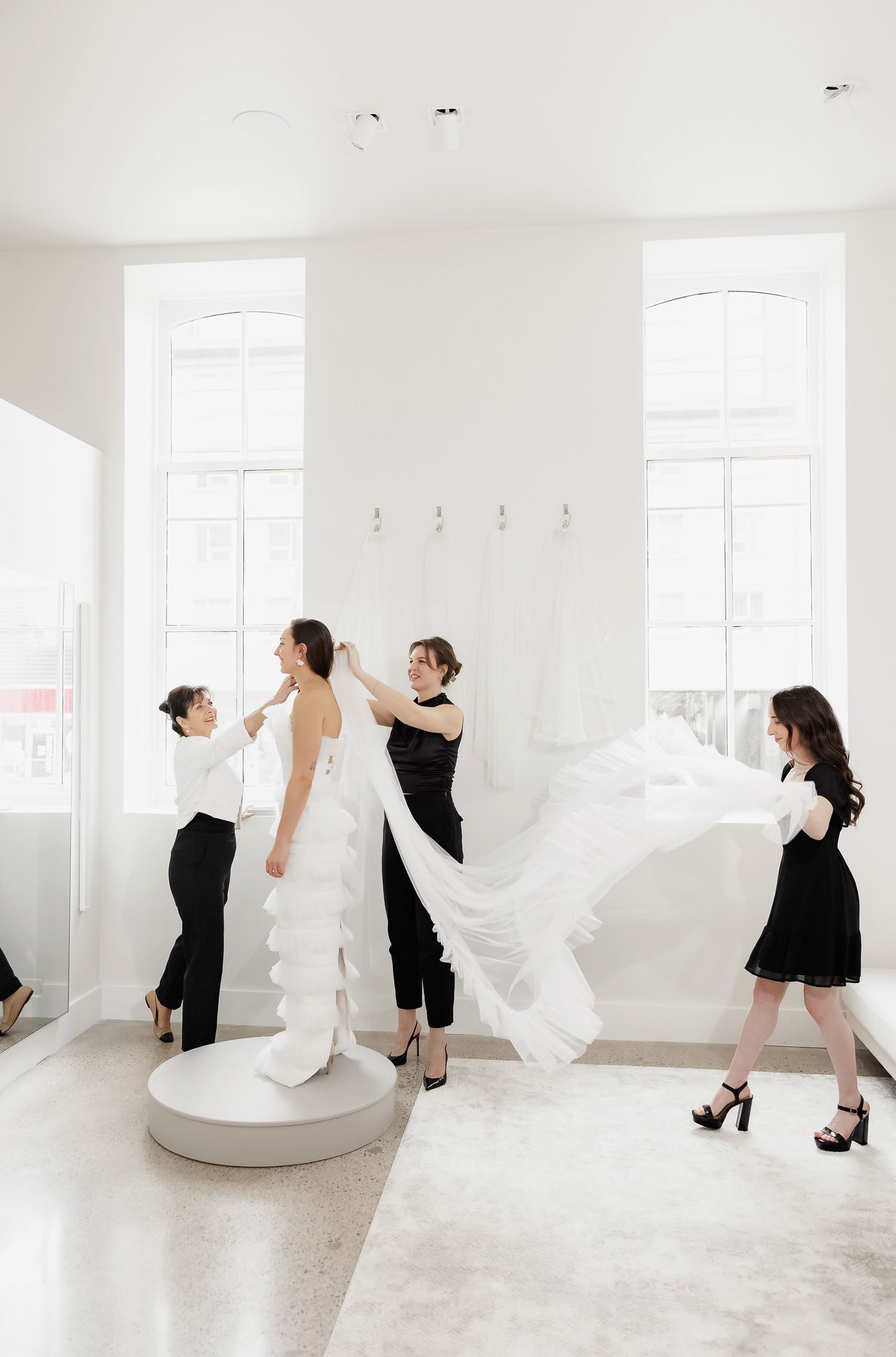 Wedding dress fitting scene with stylists arranging the flowing train on a circular platform.