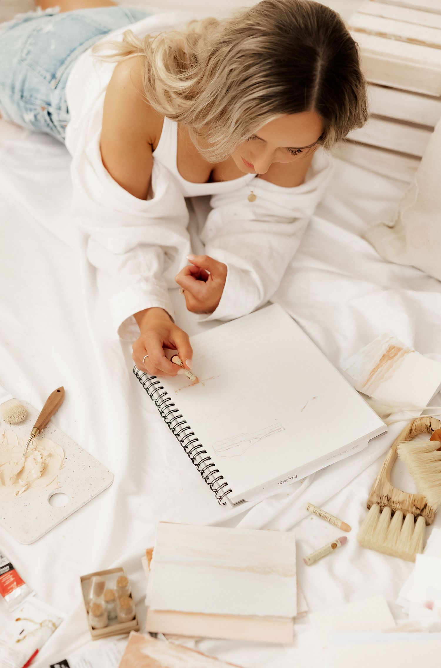 Artist working on creative project with notebook and art supplies on white surface.