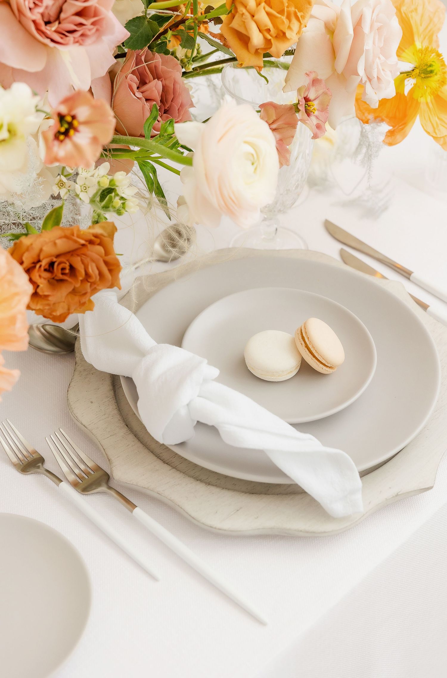 White table setting with folded napkins, macarons and spring floral decor in soft peach tones.