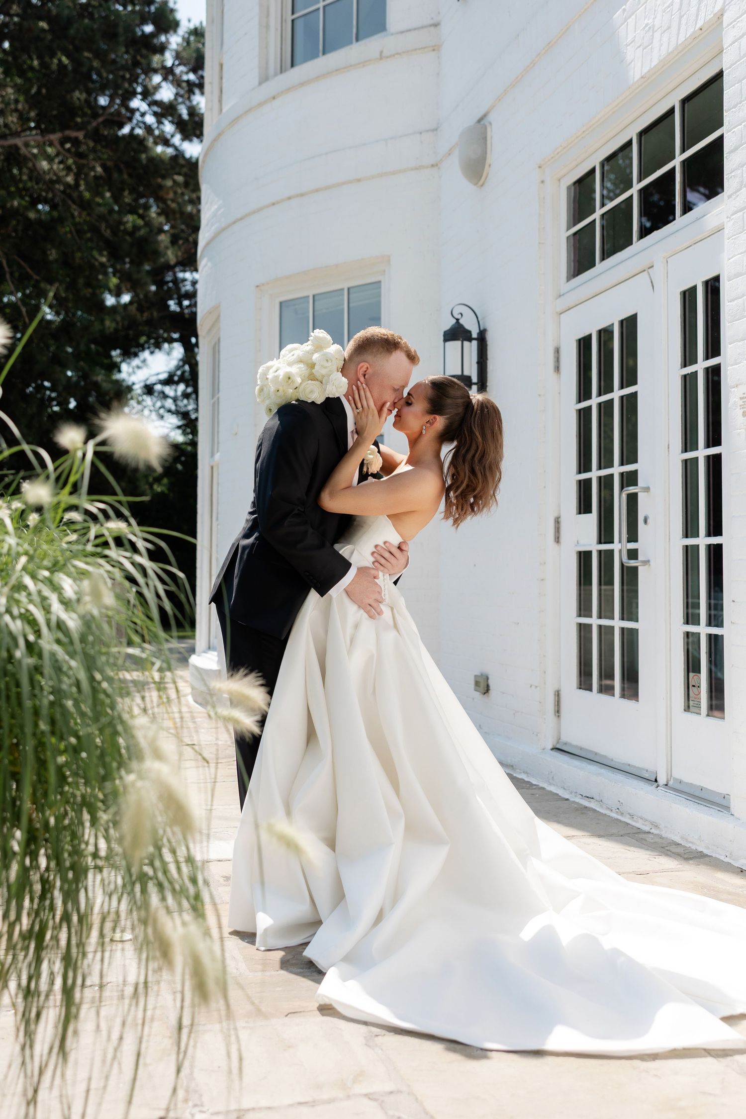 Romantic wedding couple embracing outside white building with French doors and garden elements.