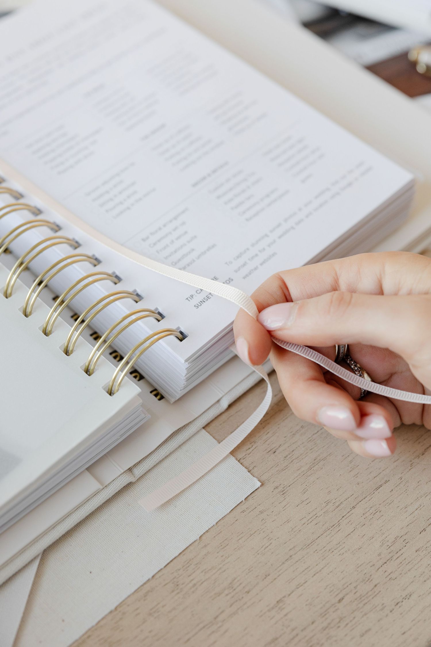 Close-up of hands writing in spiral notebook with gold binding on wooden surface.