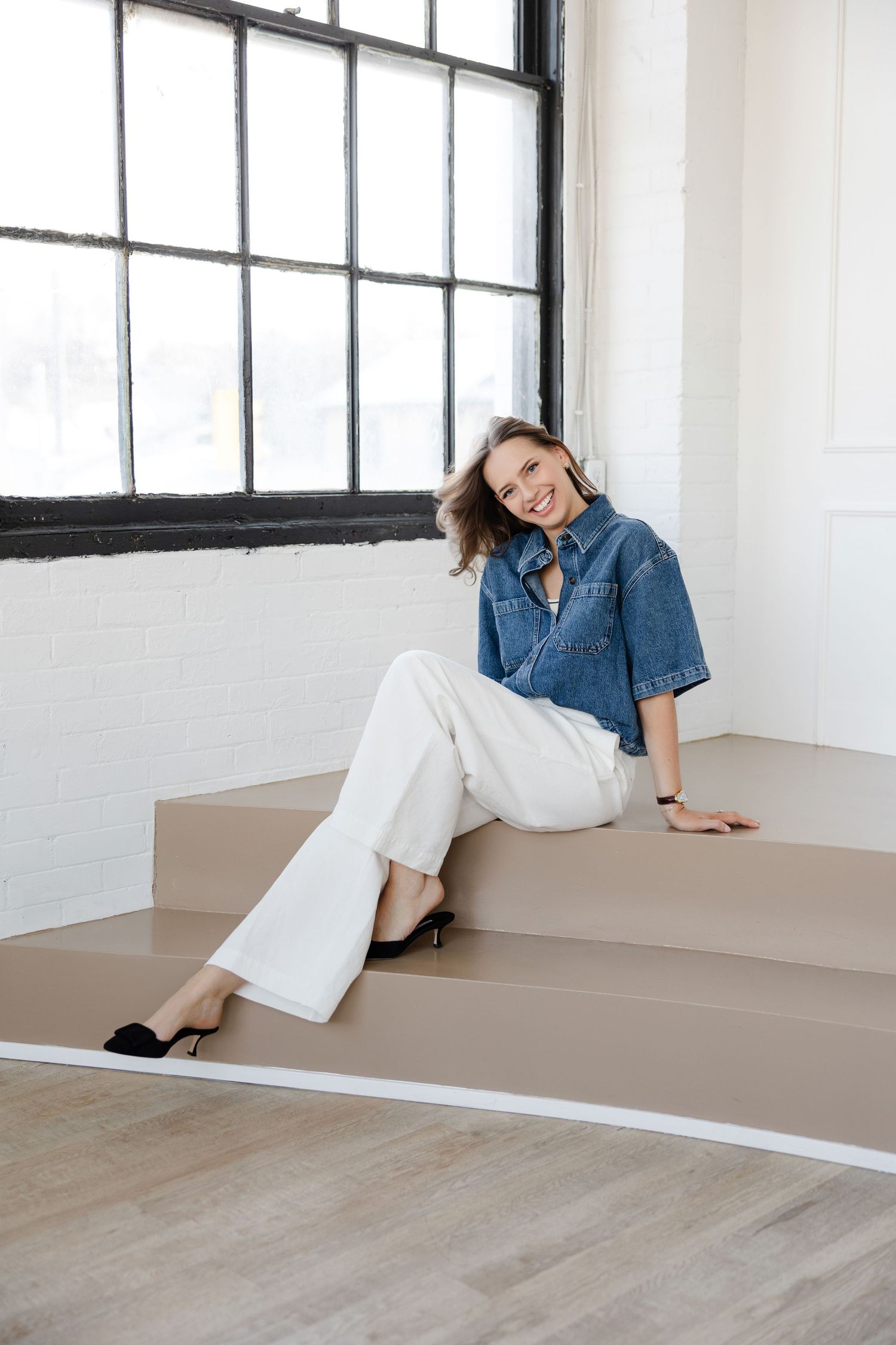 Casual portrait on steps wearing denim shirt and white pants with black shoes.