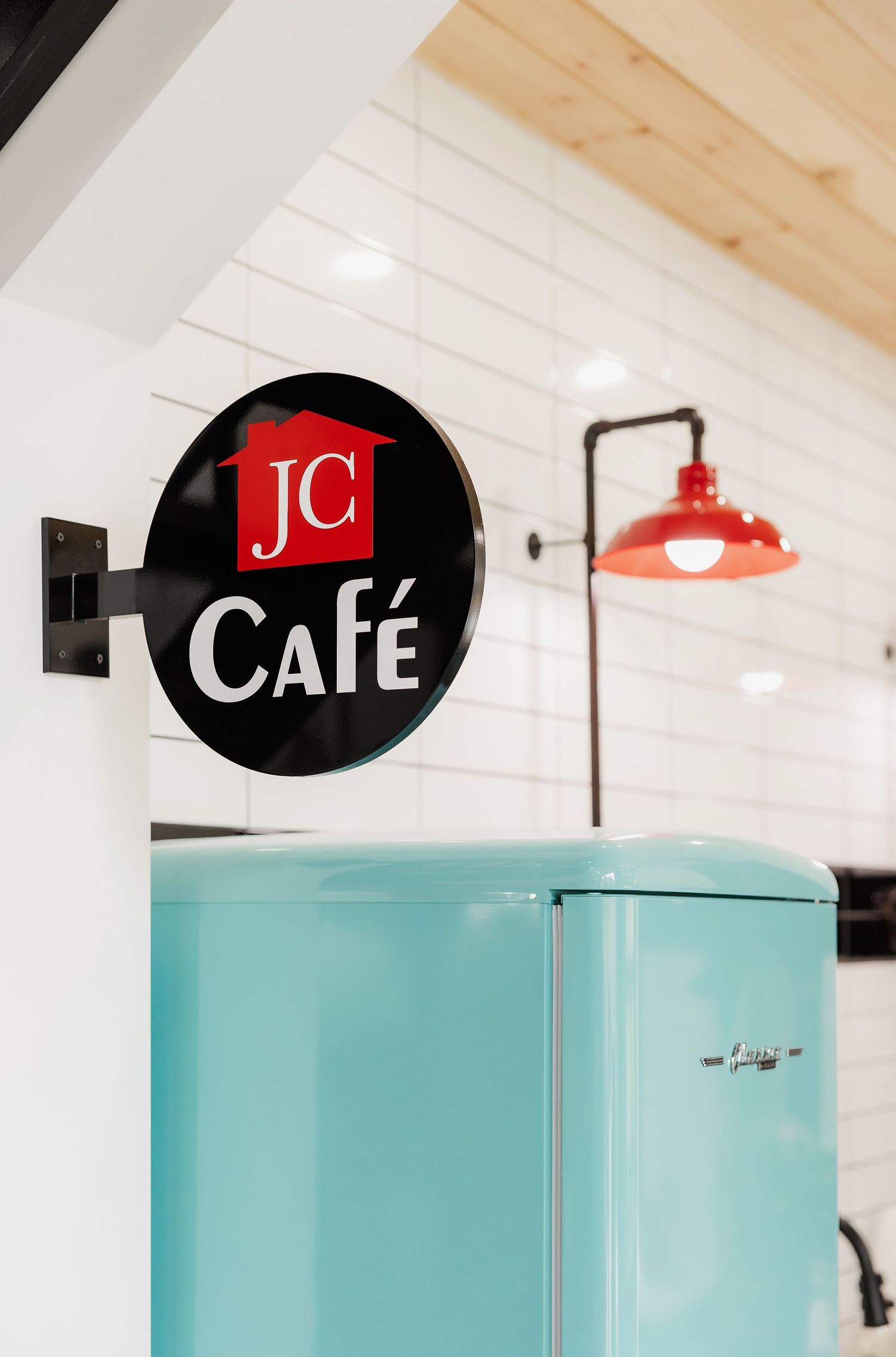 JC Cafe sign mounted on white wall next to retro turquoise refrigerator.