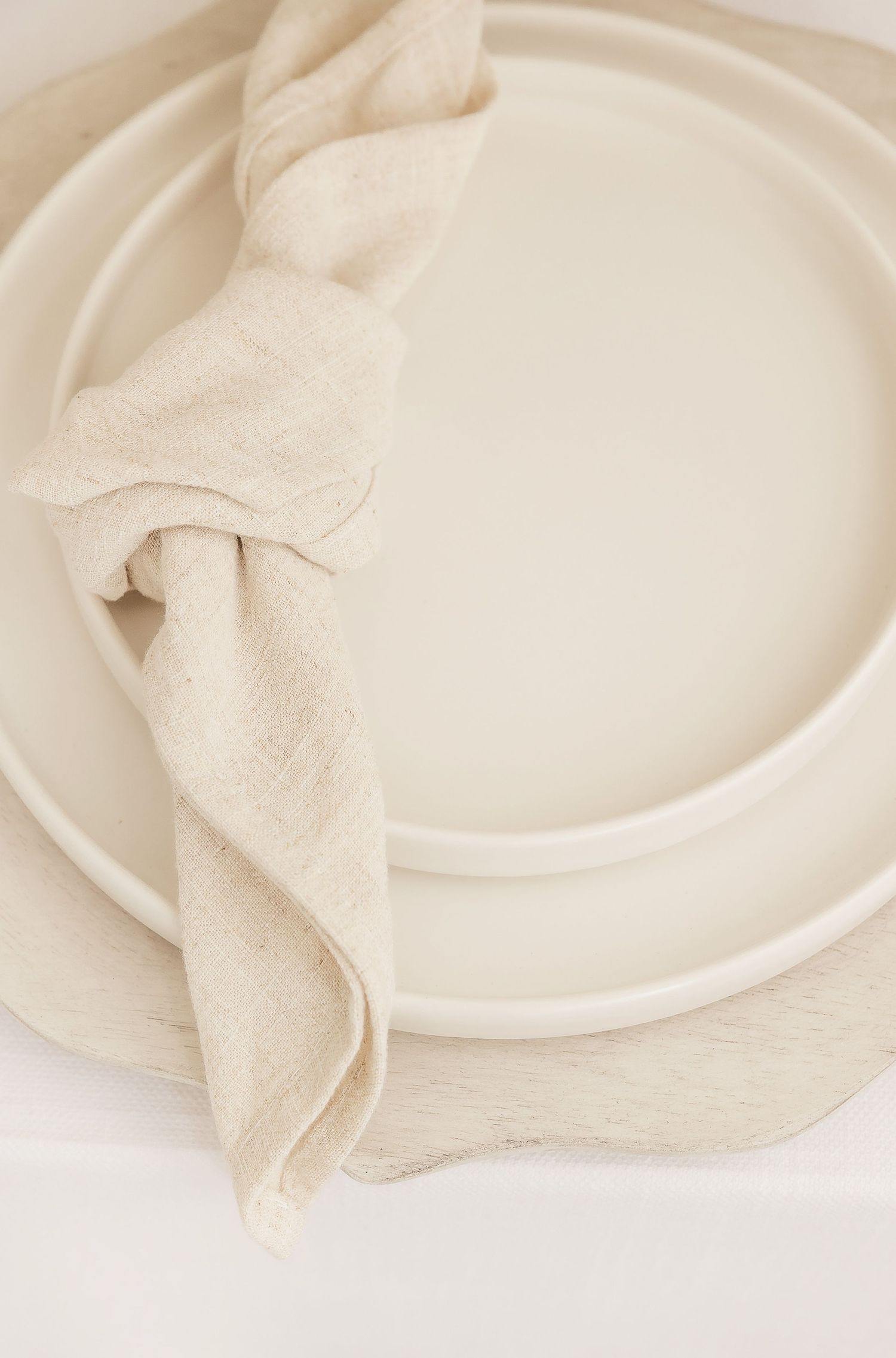 Minimalist white place setting with textured linen napkin draped across stacked plates.