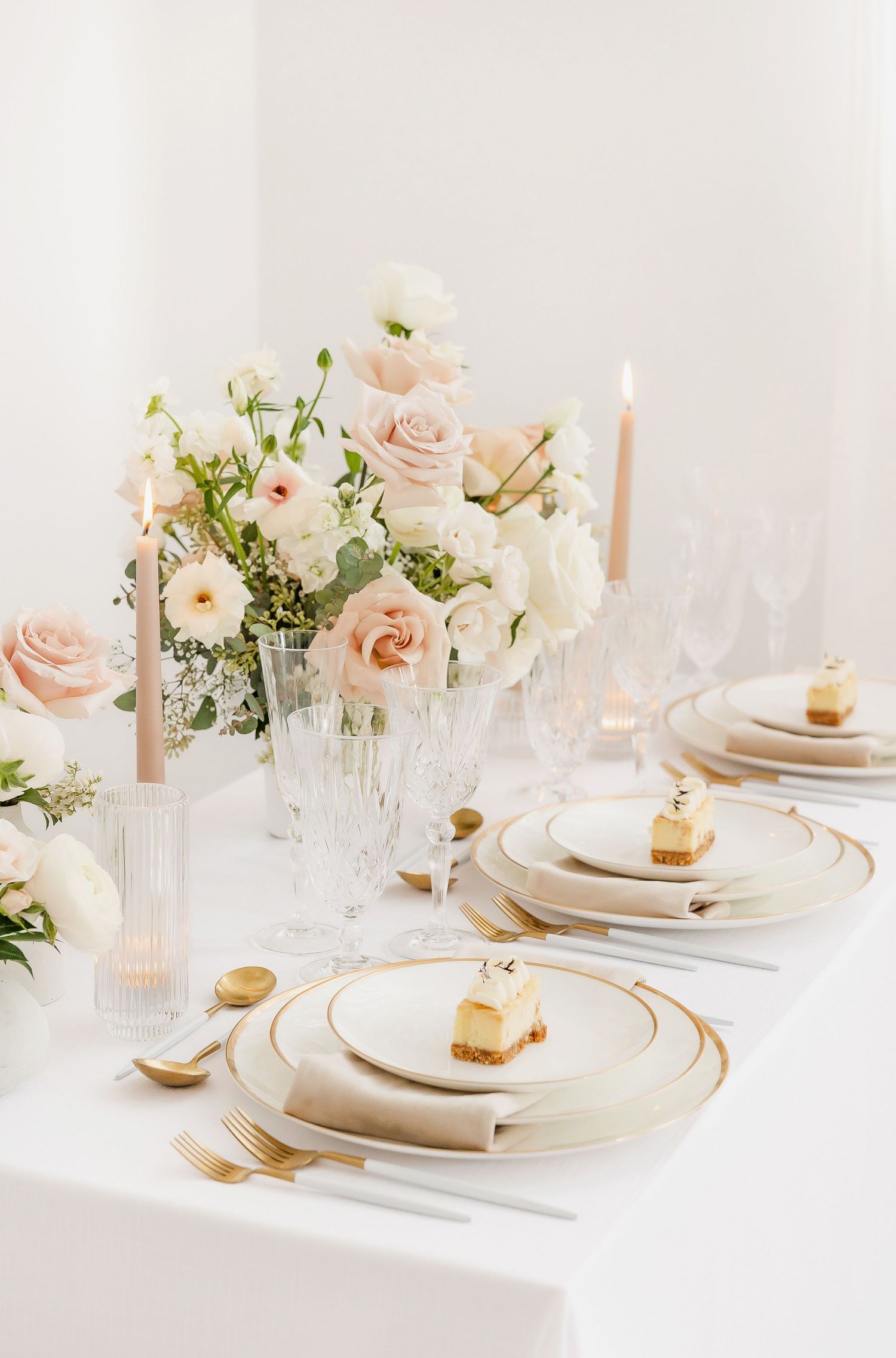 Luxurious white and gold table setting with blush roses and lit candles creating an elegant atmosphere.