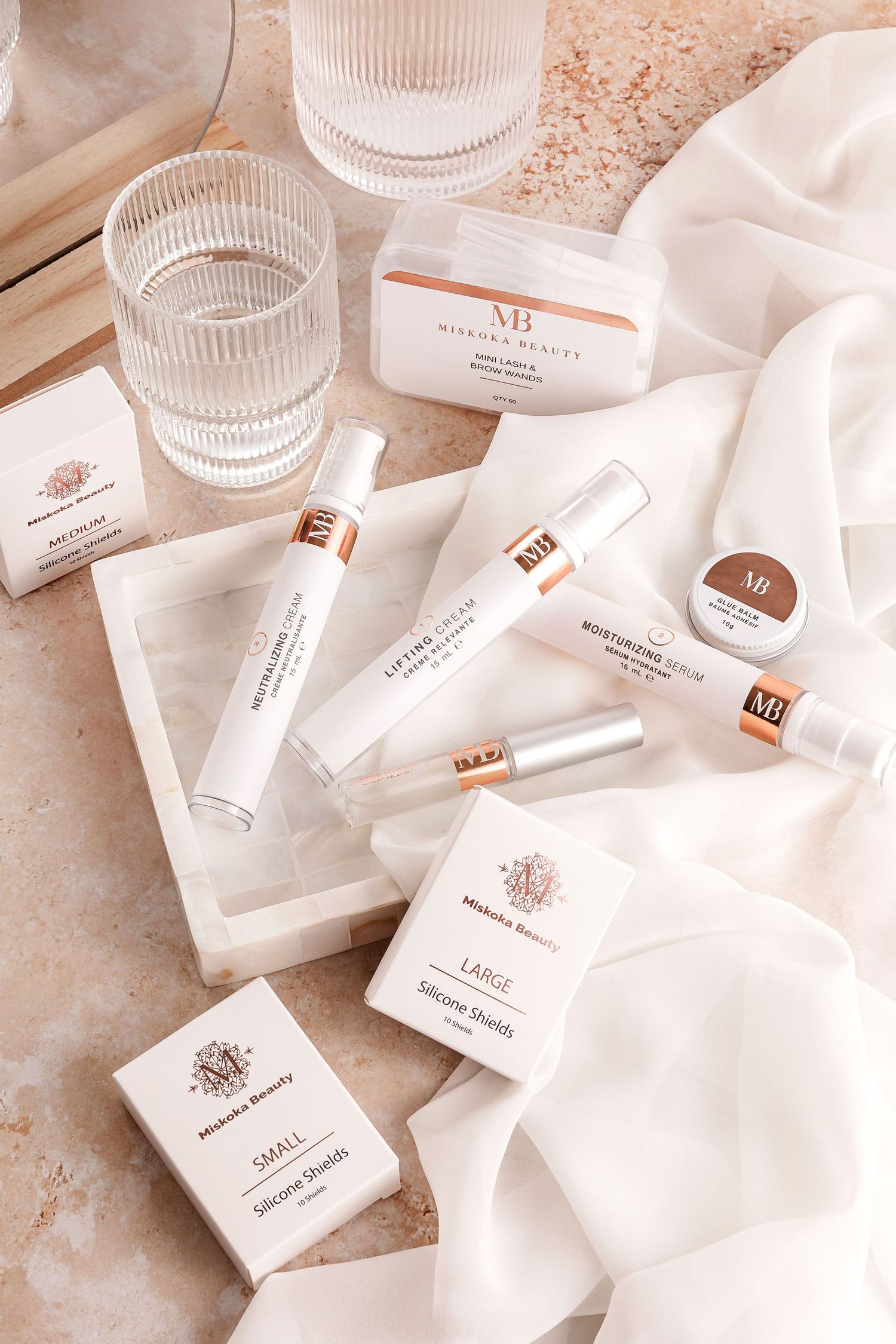 Collection of white and rose gold skincare products arranged with glass accessories.
