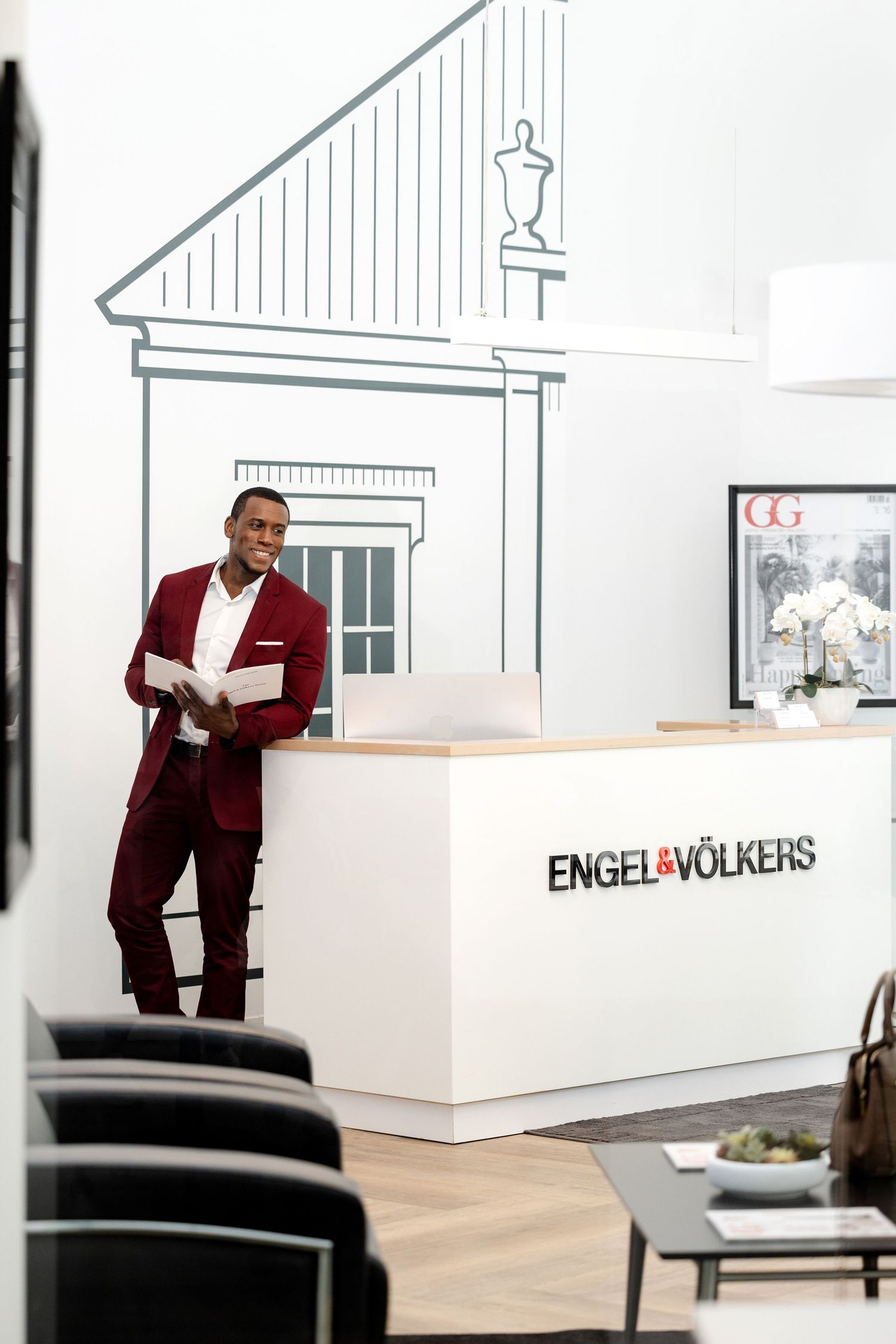 Professional real estate office interior with modern white reception desk and burgundy accents.