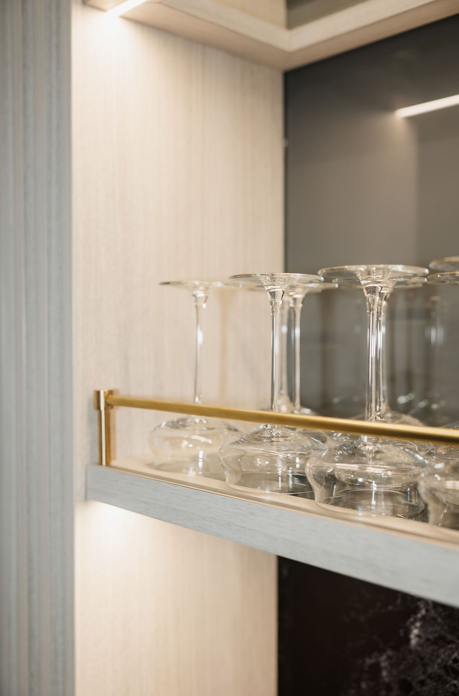 Row of empty cocktail glasses displayed on modern white shelving against a gray wall.