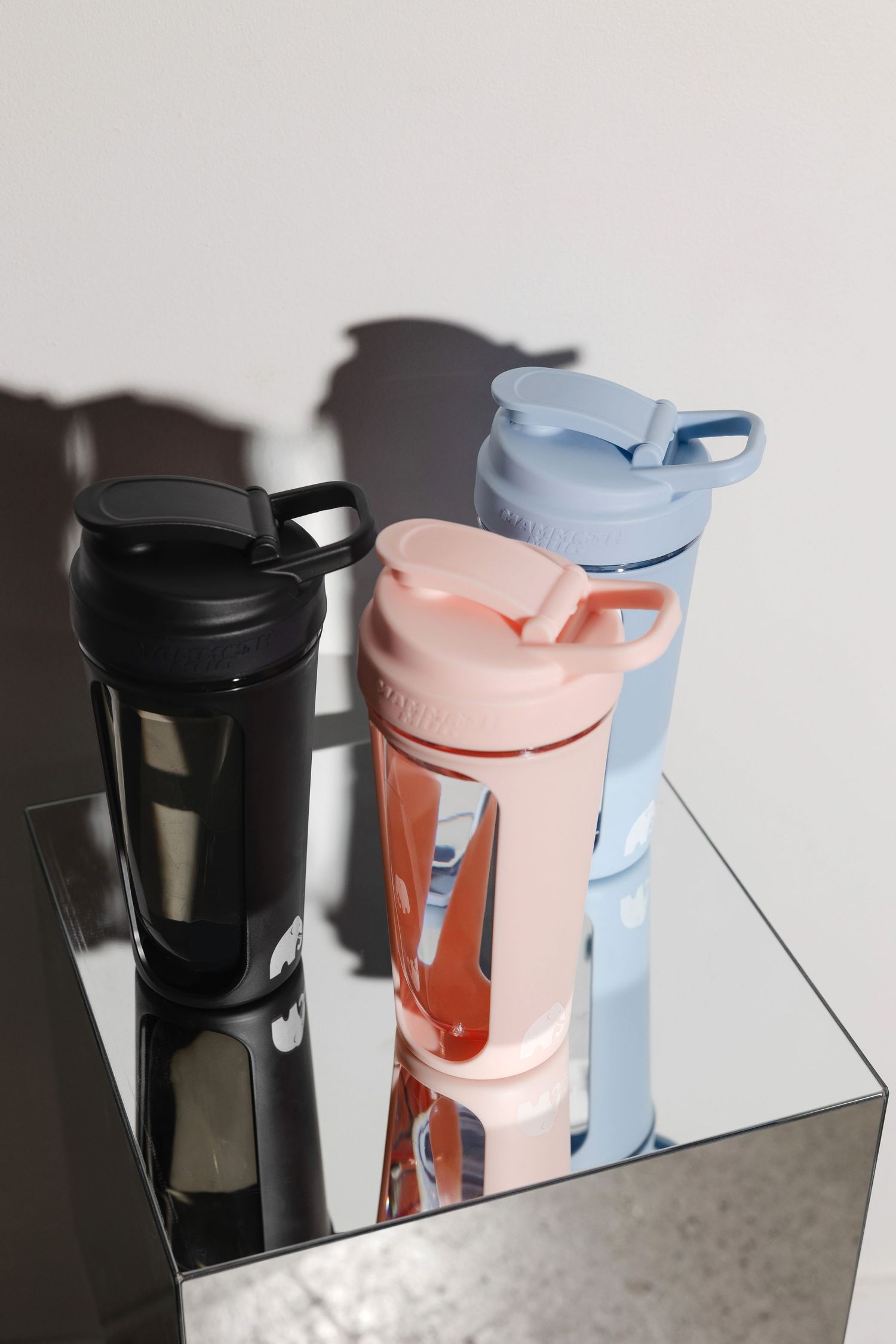 Collection of water bottles in black, pink and light blue colors displayed on reflective surface.