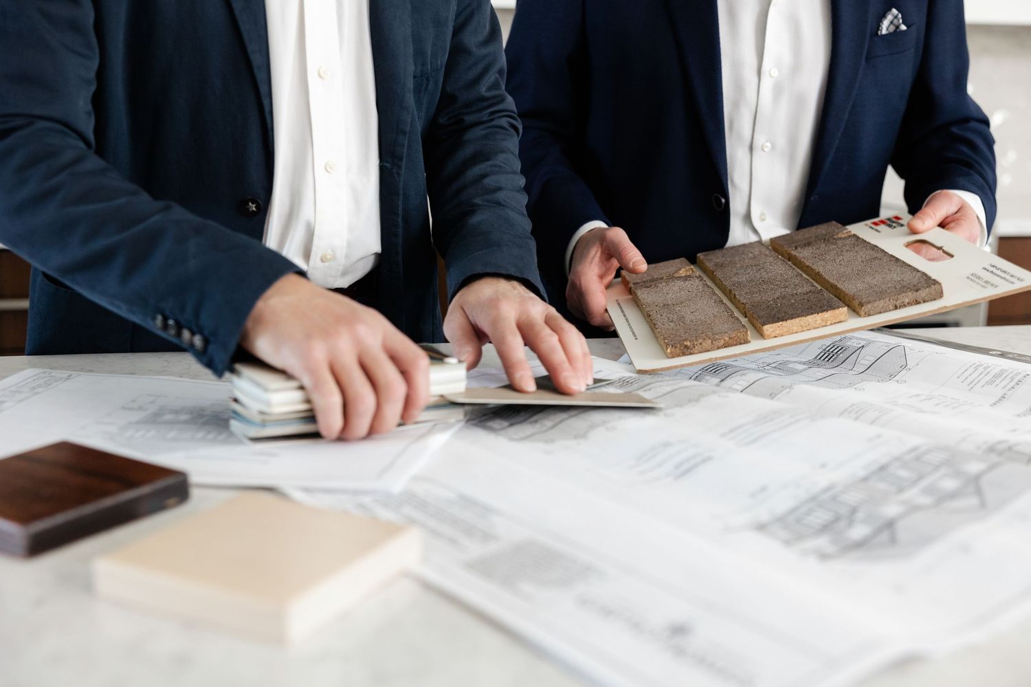 Team of executives in navy suits examining blueprints on conference table.