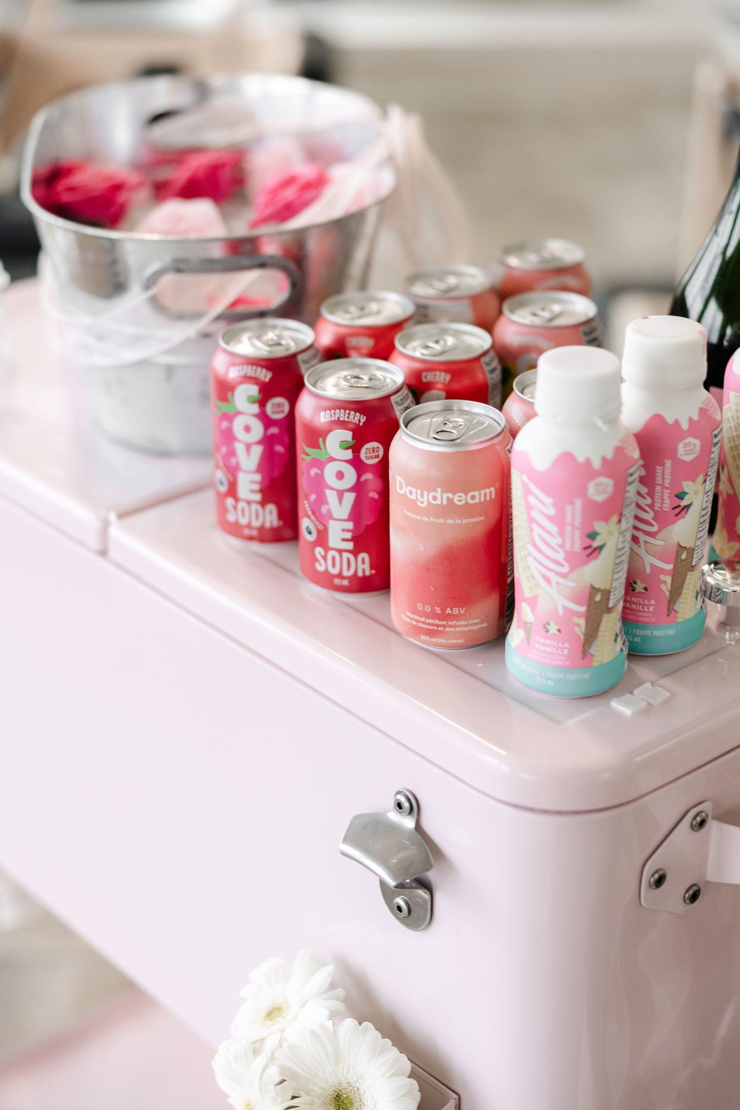 Pink and white soda cans arranged on a pastel cooler at fitness event.