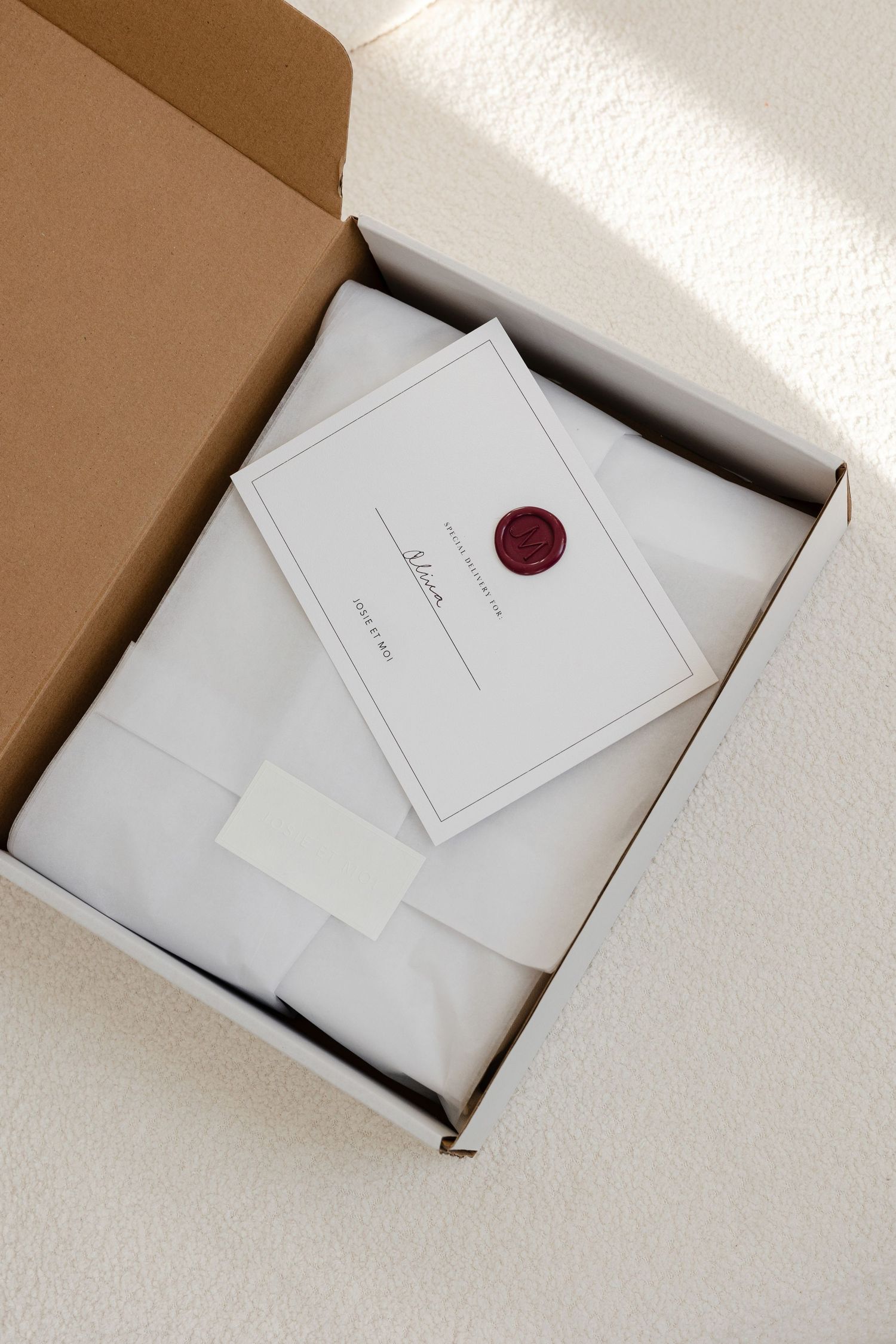 Elegant white packaging with red wax seal displayed in brown shipping box.
