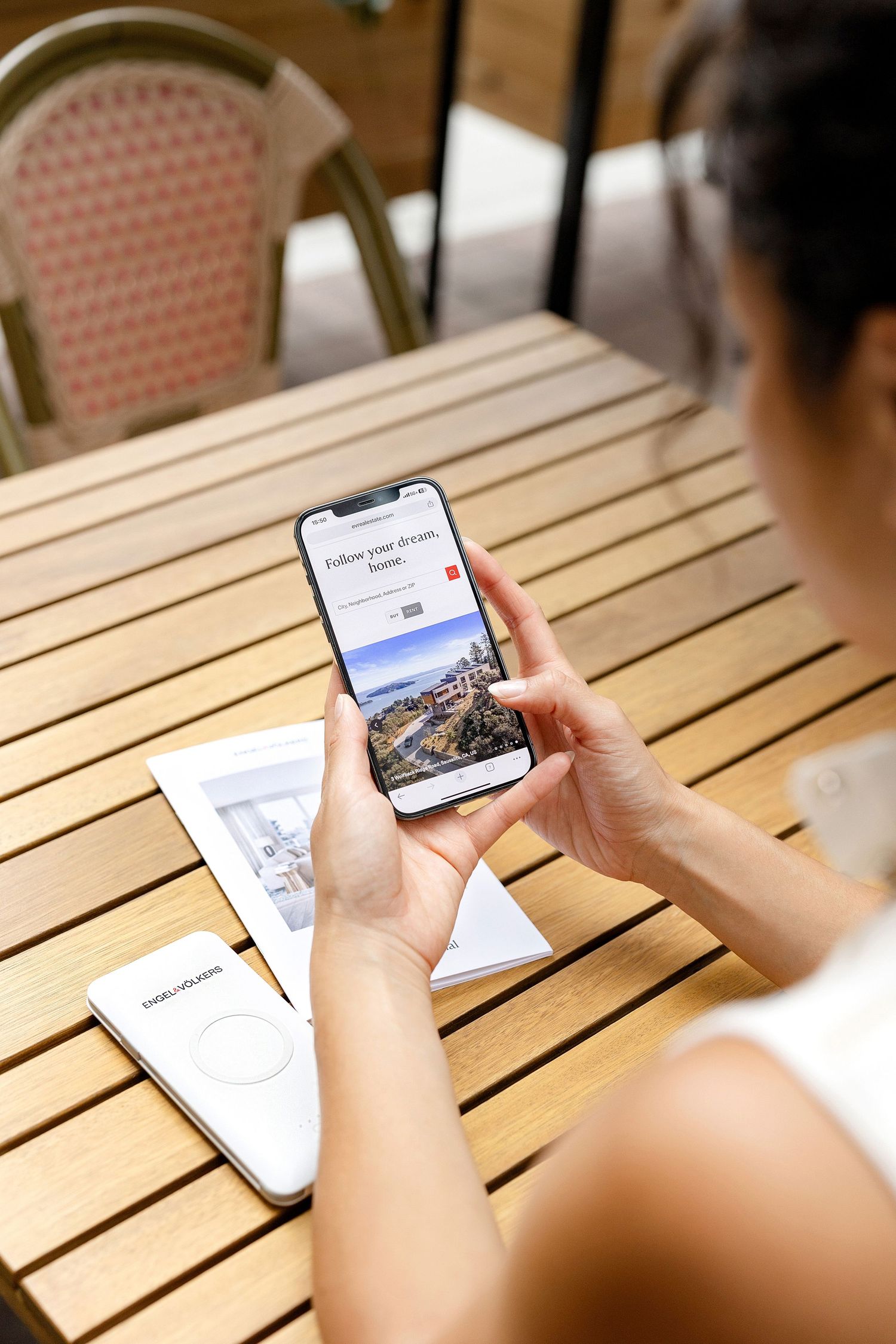 Hands holding a smartphone displaying content while sitting at a wooden table.