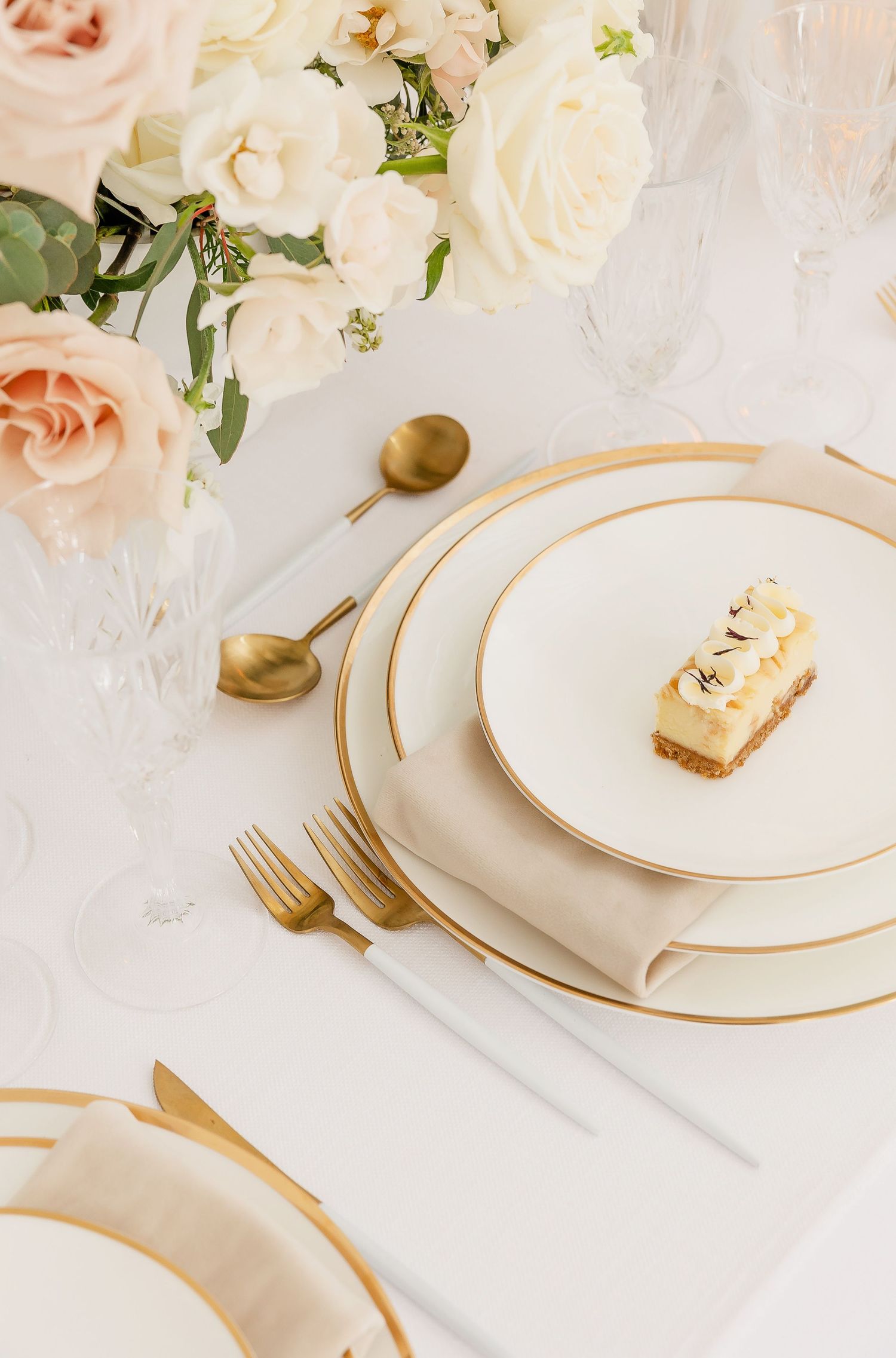 Elegant white and gold place settings adorned with blush roses and petite desserts.