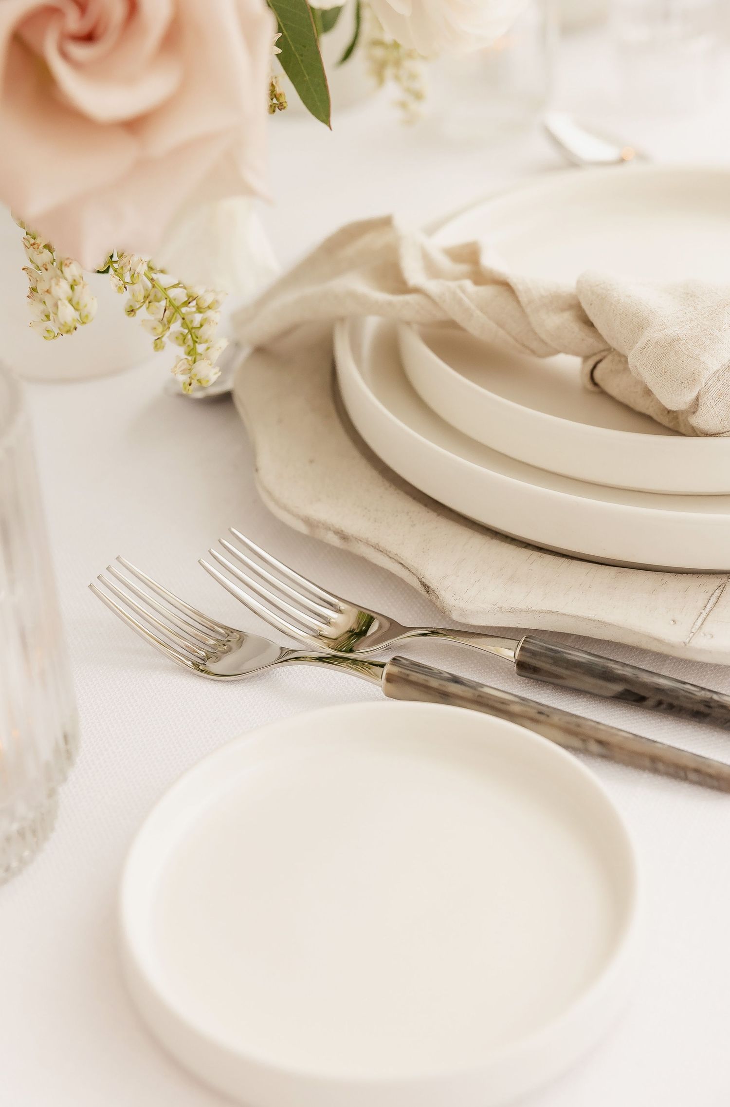 Vintage silverware beside white plates with soft pink roses and delicate greenery.