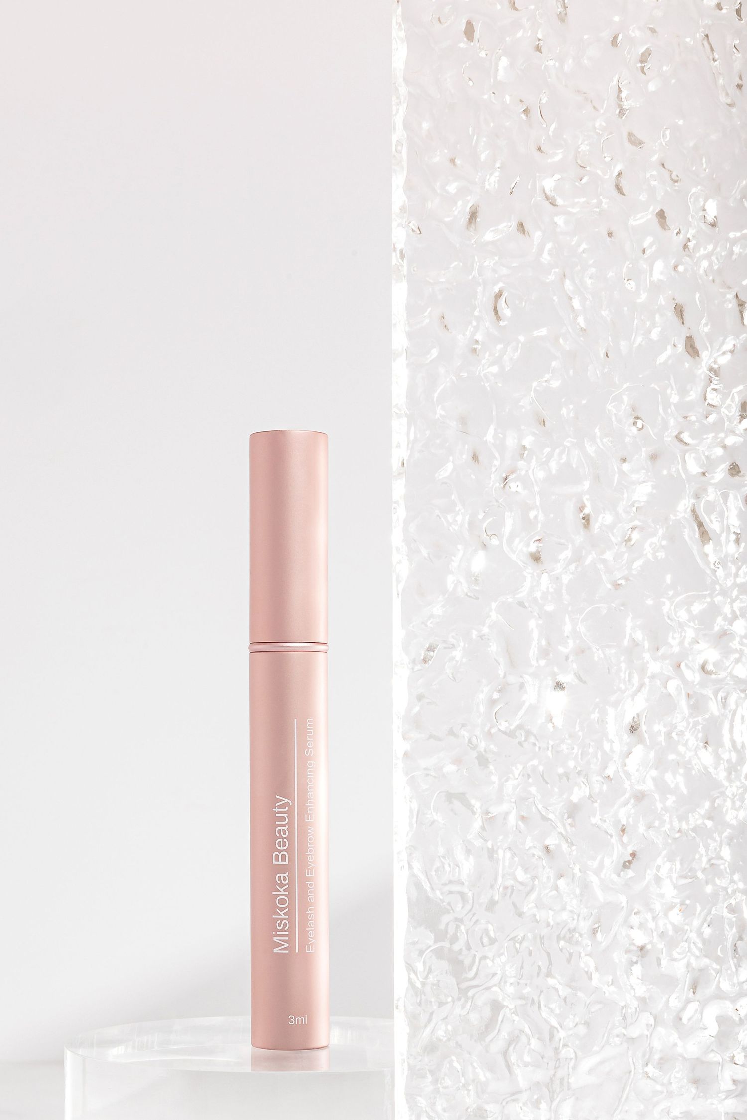 Rose gold beauty product bottle against textured white background with sparkle effect.