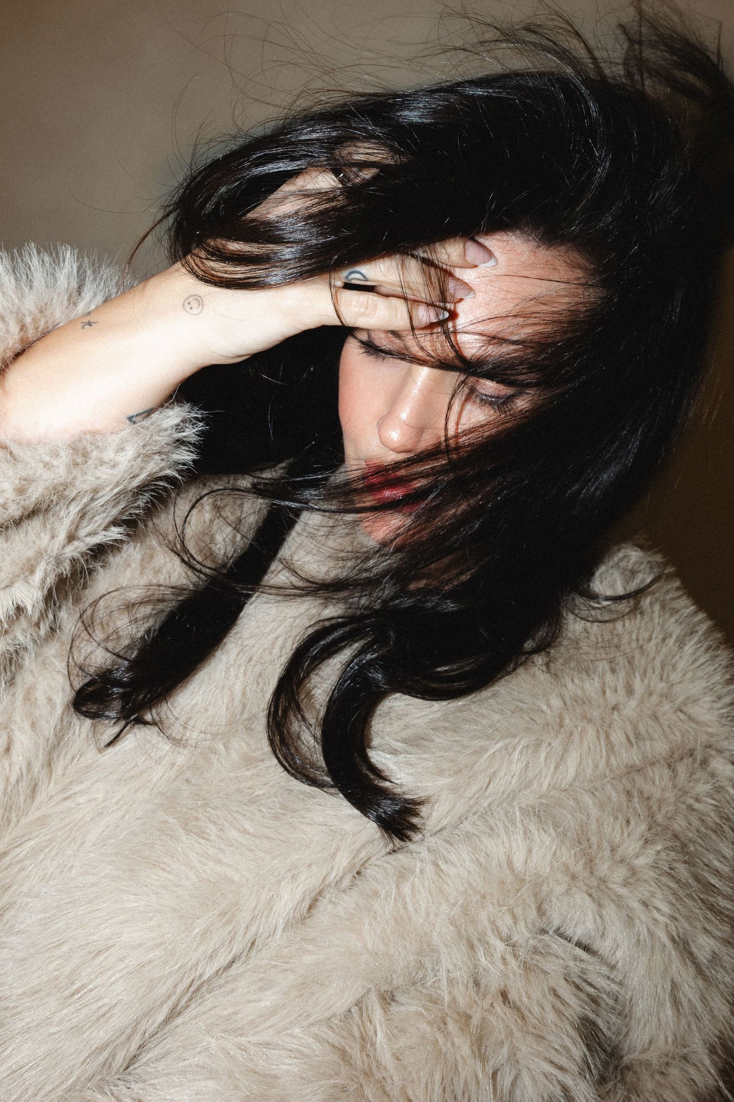 Woman in fluffy fur coat tosses dark hair dramatically during fashion photoshoot.