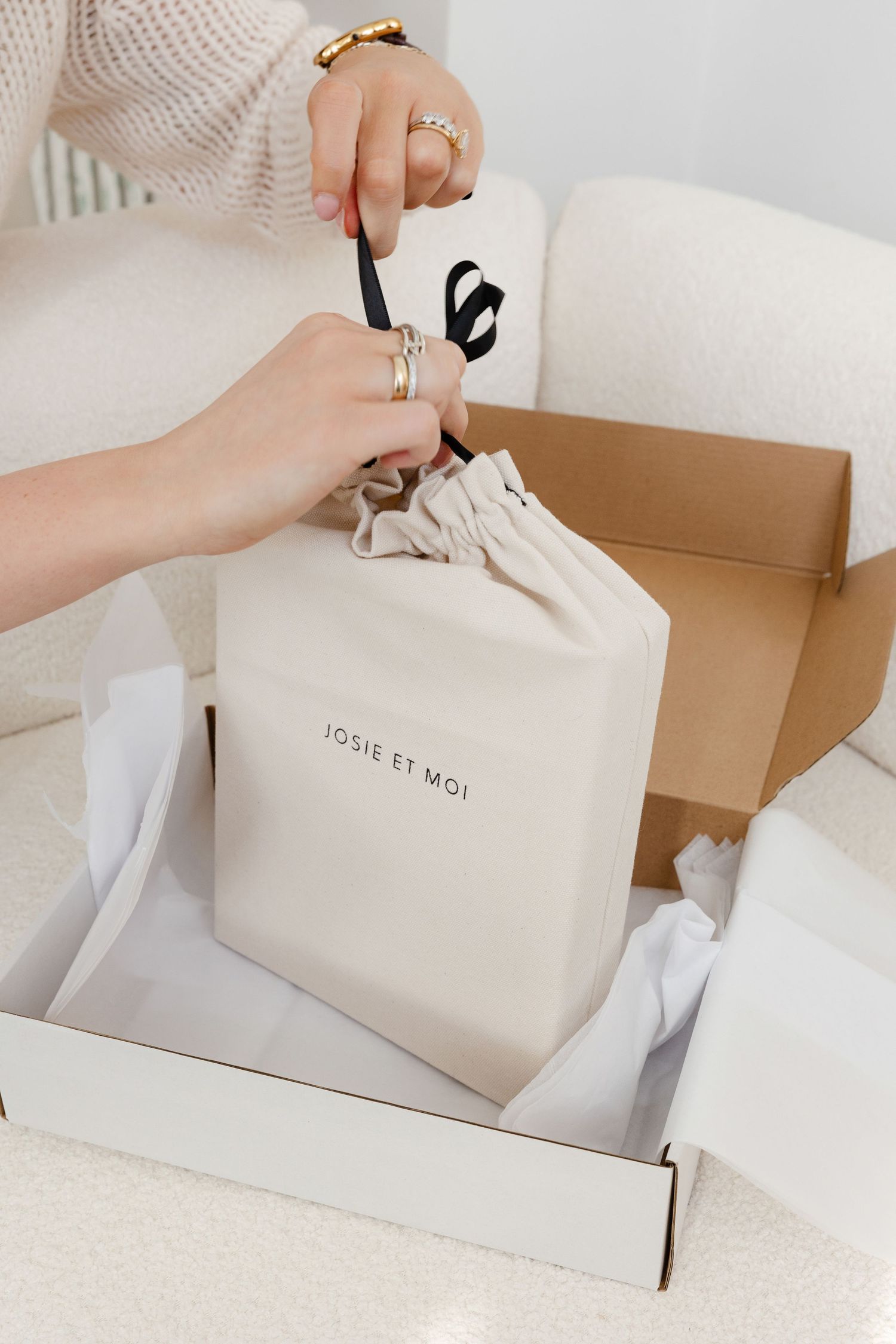 Hands arranging white branded packaging boxes and bags on a textured surface.