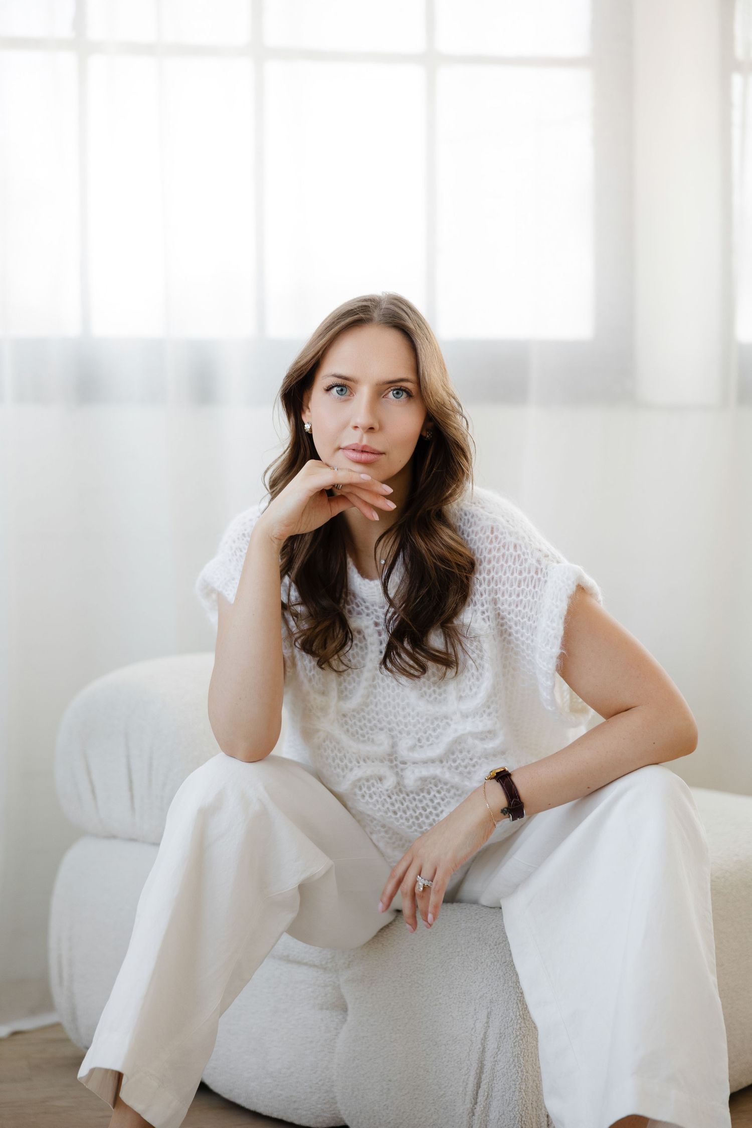 Thoughtful pose in white knit top and wide-leg pants against bright interior.