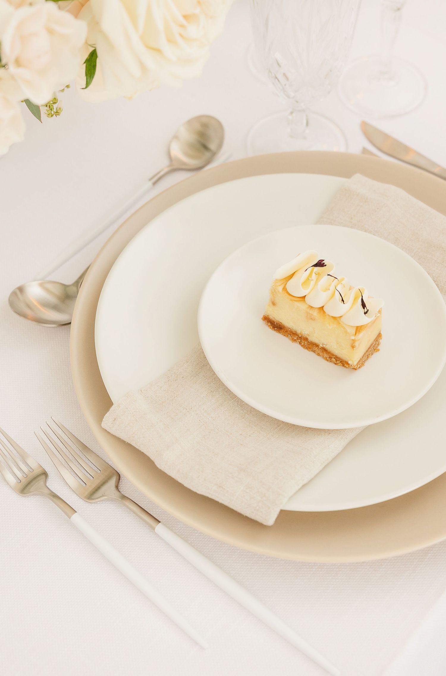 Delicate dessert presentation on white plates with cream colored linens and floral accents.