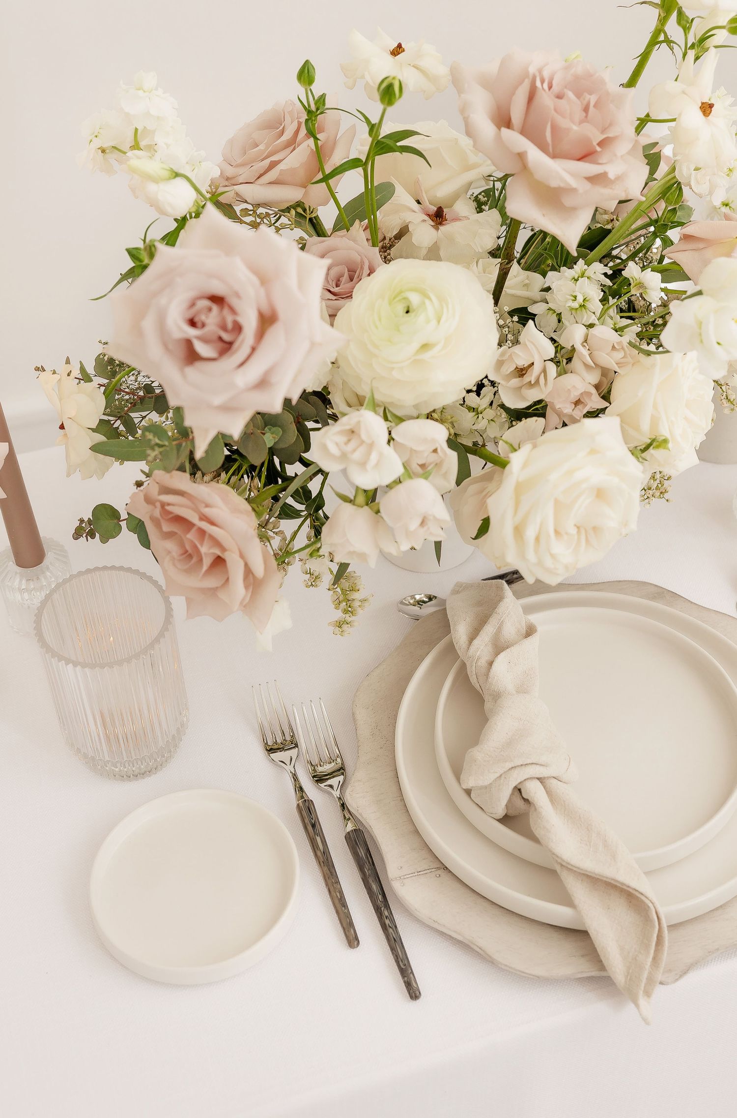 Romantic table setting with blush roses and white ranunculus in a soft, elegant arrangement.