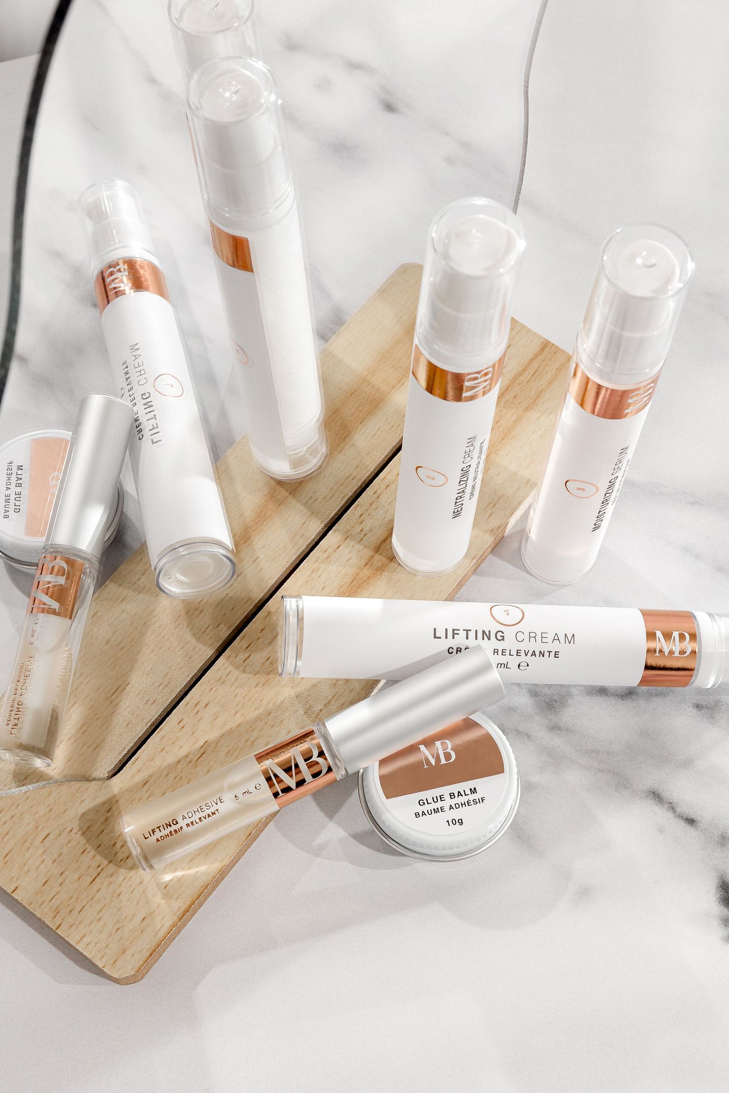 Beauty products including lifting cream and serums displayed on wooden board with marble background.