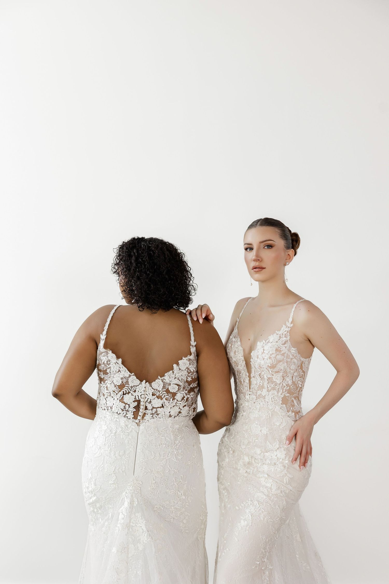 Back view of wedding gowns showing intricate lace detailing and fitted silhouettes against white backdrop.