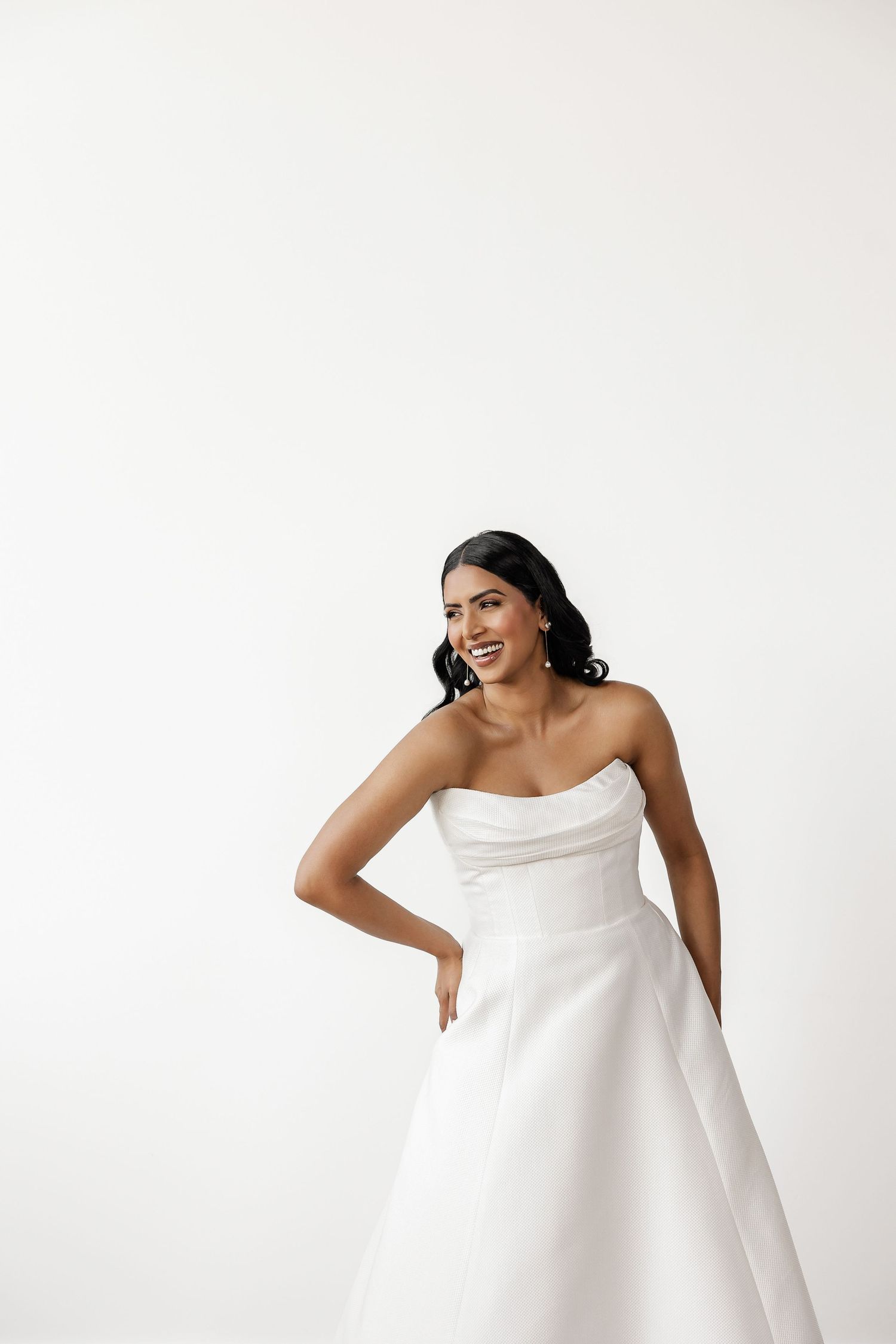 Elegant poses in flowing white asymmetrical dress against minimalist studio backdrop.