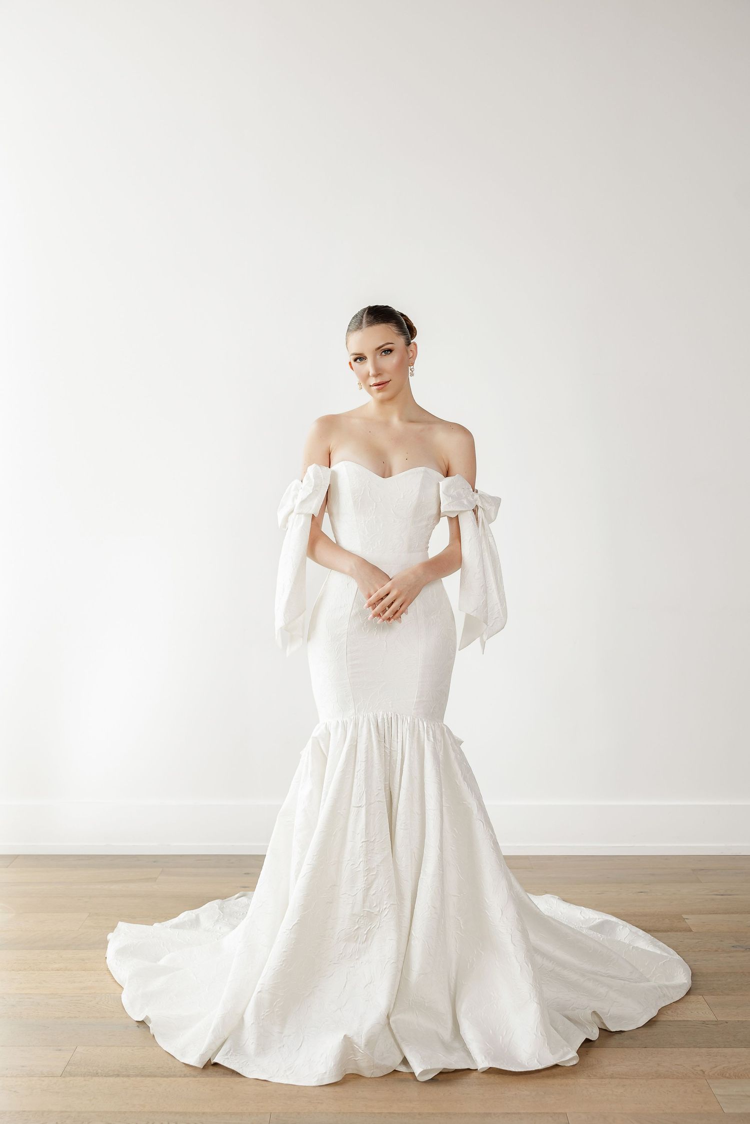 Classic white ballgown wedding dress with off-shoulder design photographed on wooden floor.