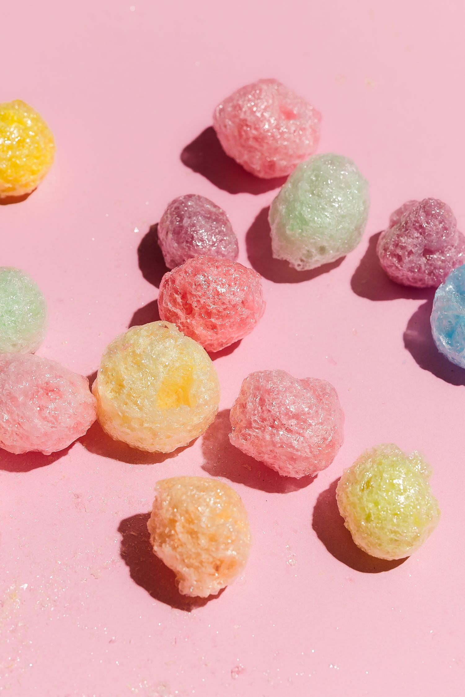 Colorful sugar-coated gummy candies arranged on a pink background.
